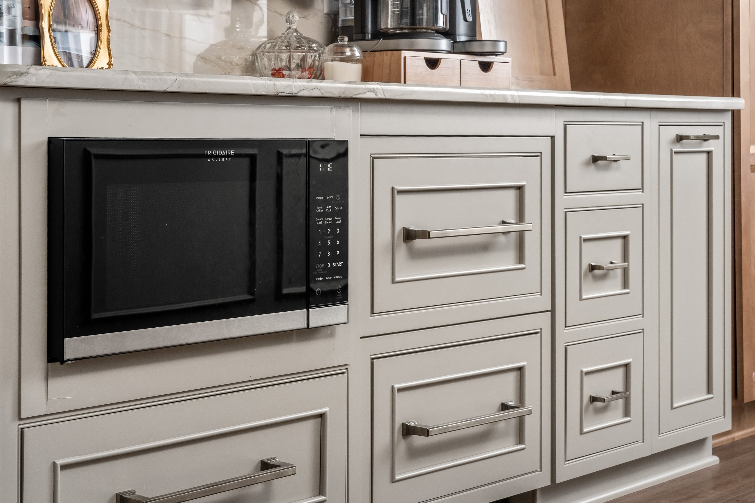 A black and silver microwave oven built into a white kitchen cabinet with drawers and a marble countertop.