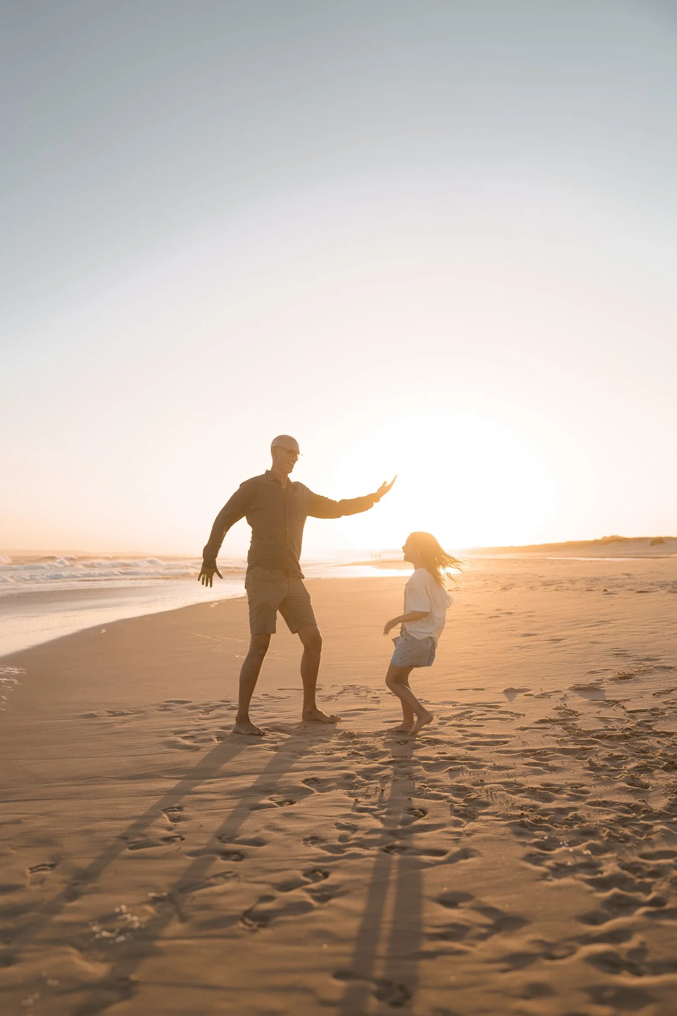 A man and a girl playing on the beach during sunset.