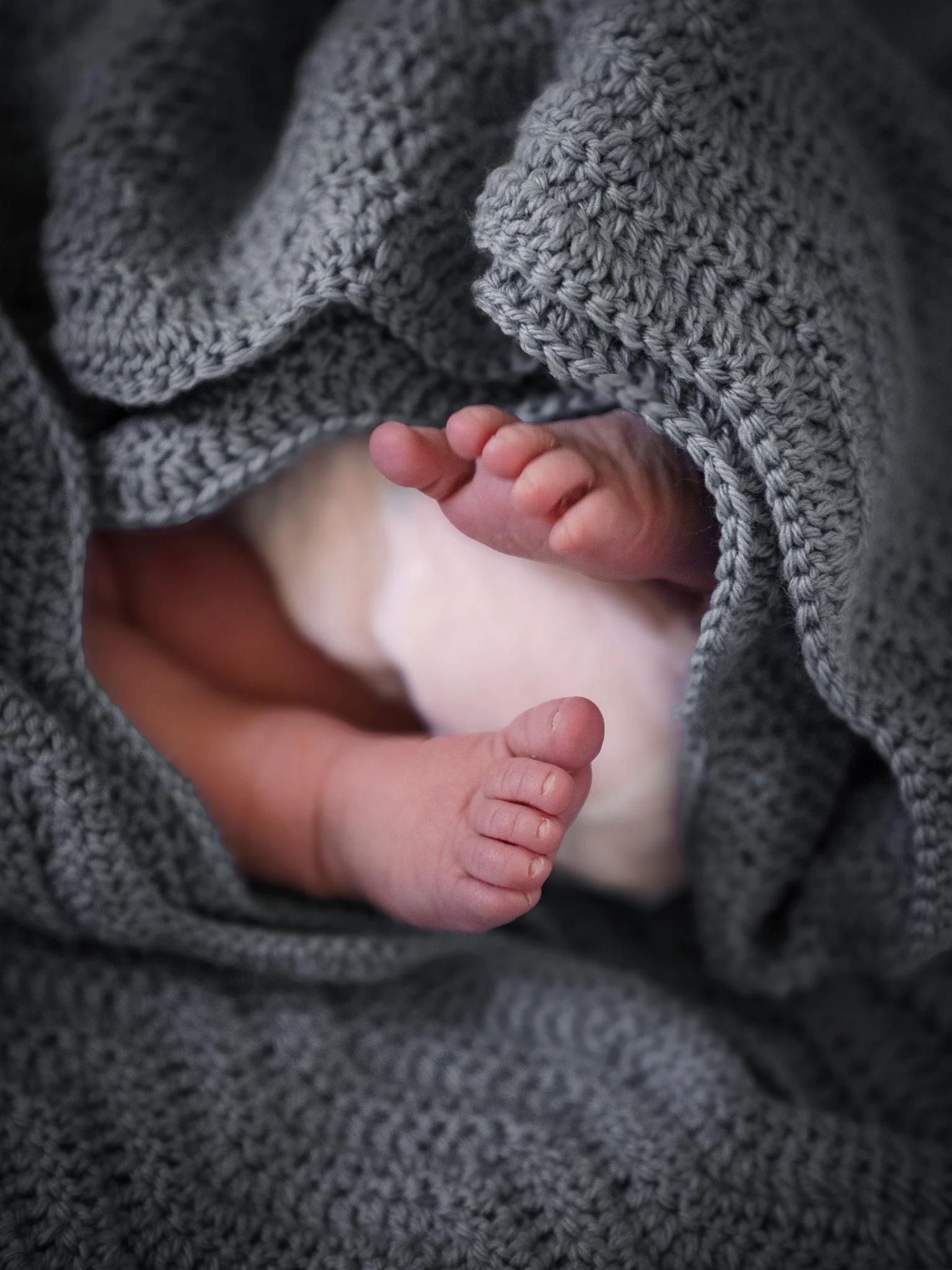 Close-up of a newborn baby’s tiny feet, wrapped in a gray knitted blanket.