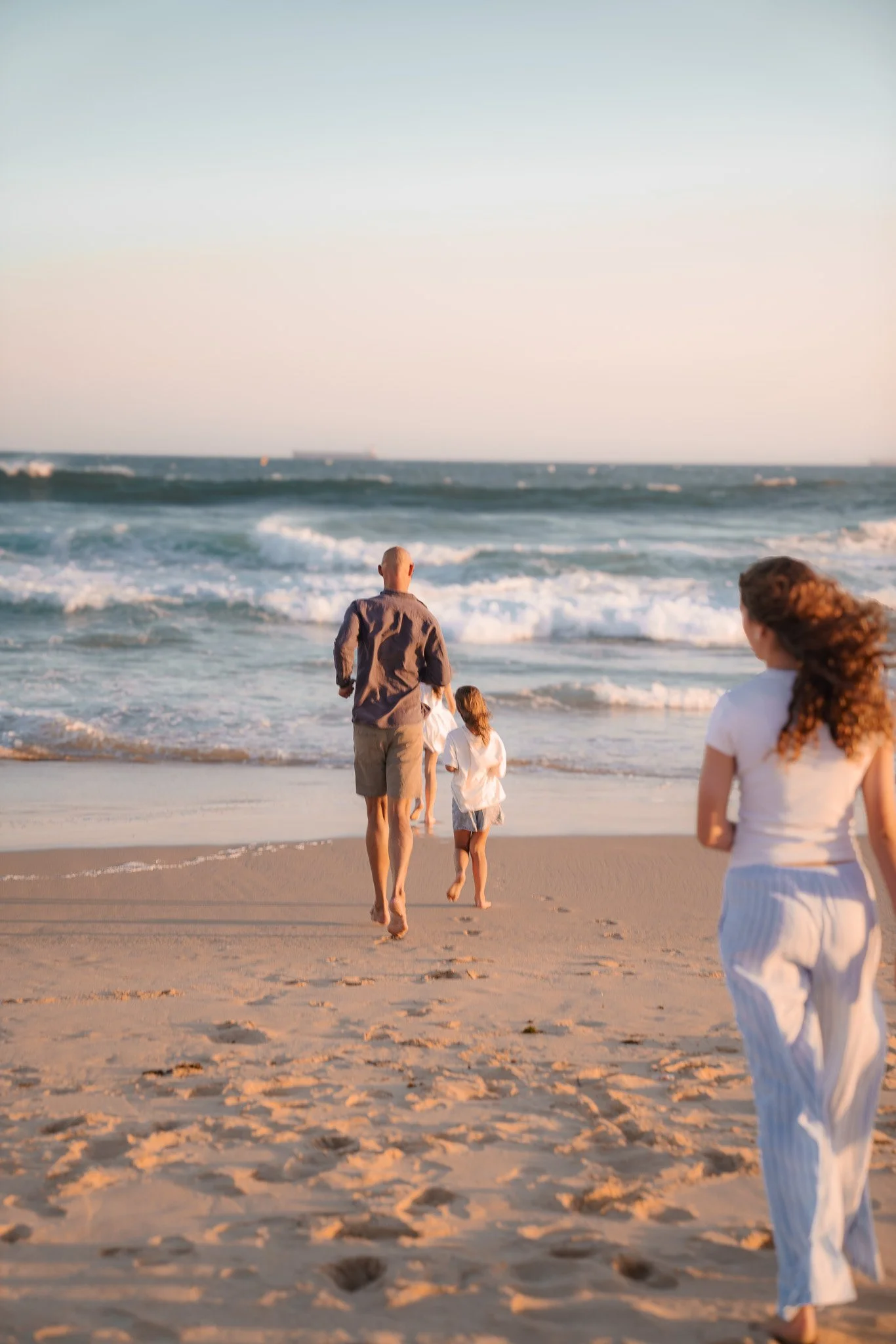 Family walking on the beach during sunset, with waves crashing on the shore.