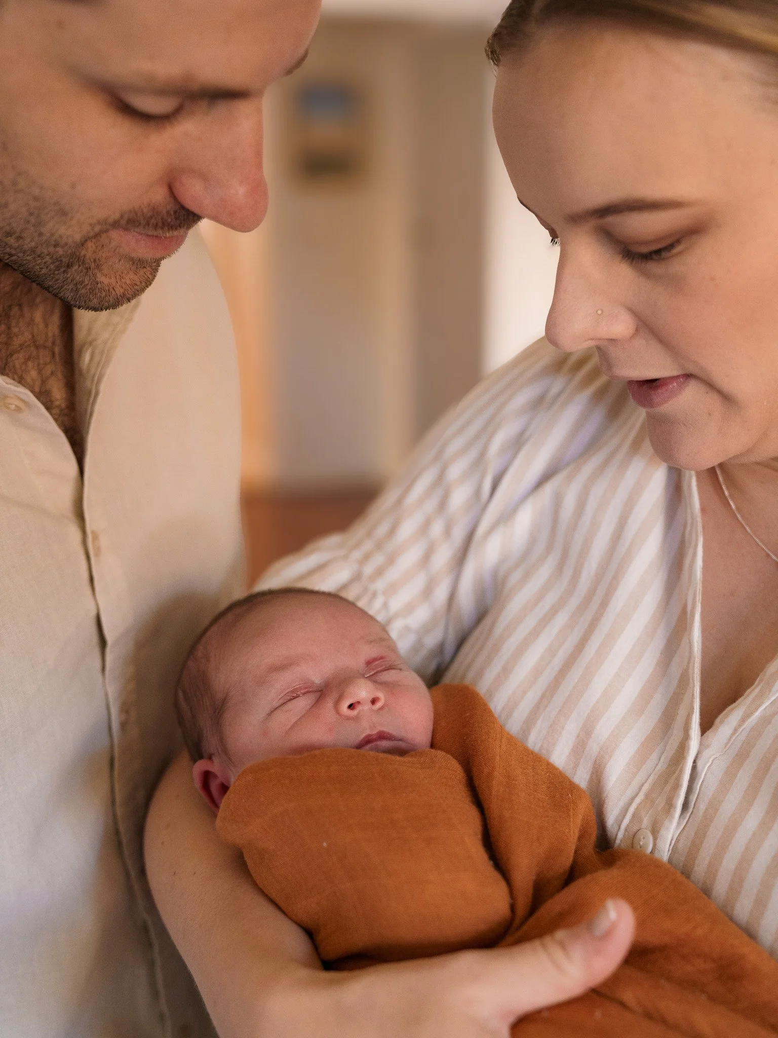 A couple holding a sleeping newborn baby wrapped in an orange blanket.