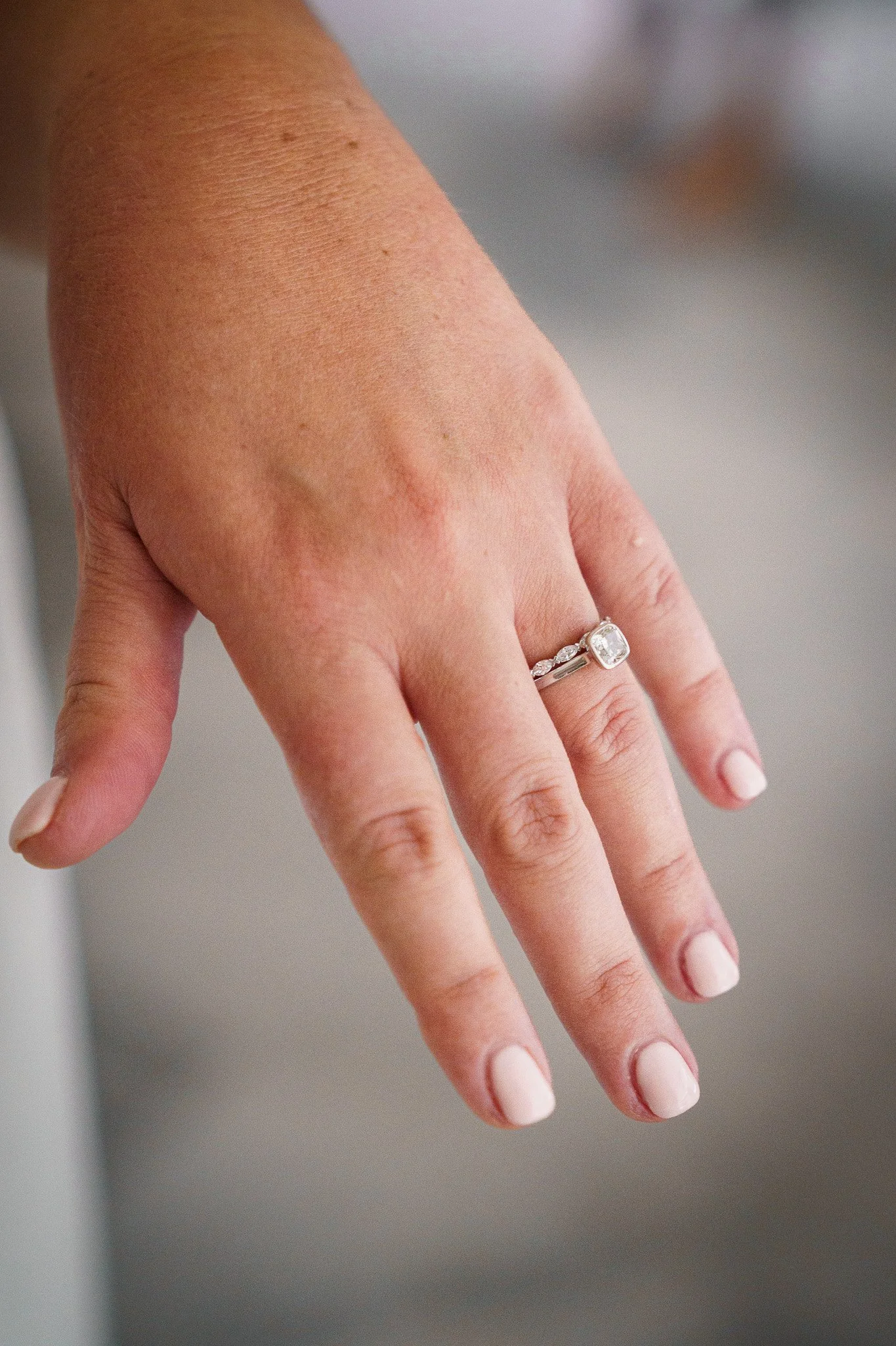 Close-up of a woman's left hand showing a large square-cut engagement ring with a diamond center stone and a wedding band with smaller diamonds.