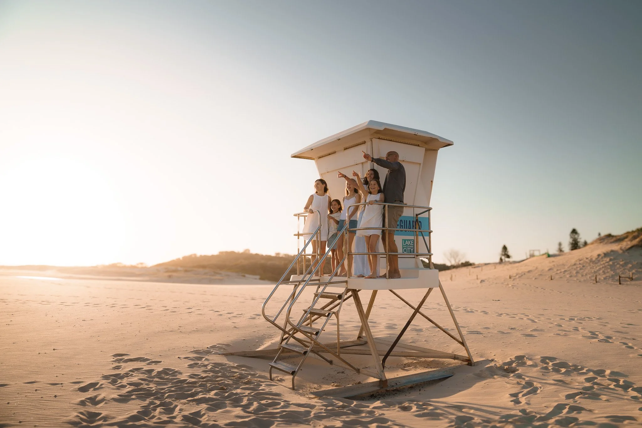 Family on a lifeguard tower on the beach during sunset.