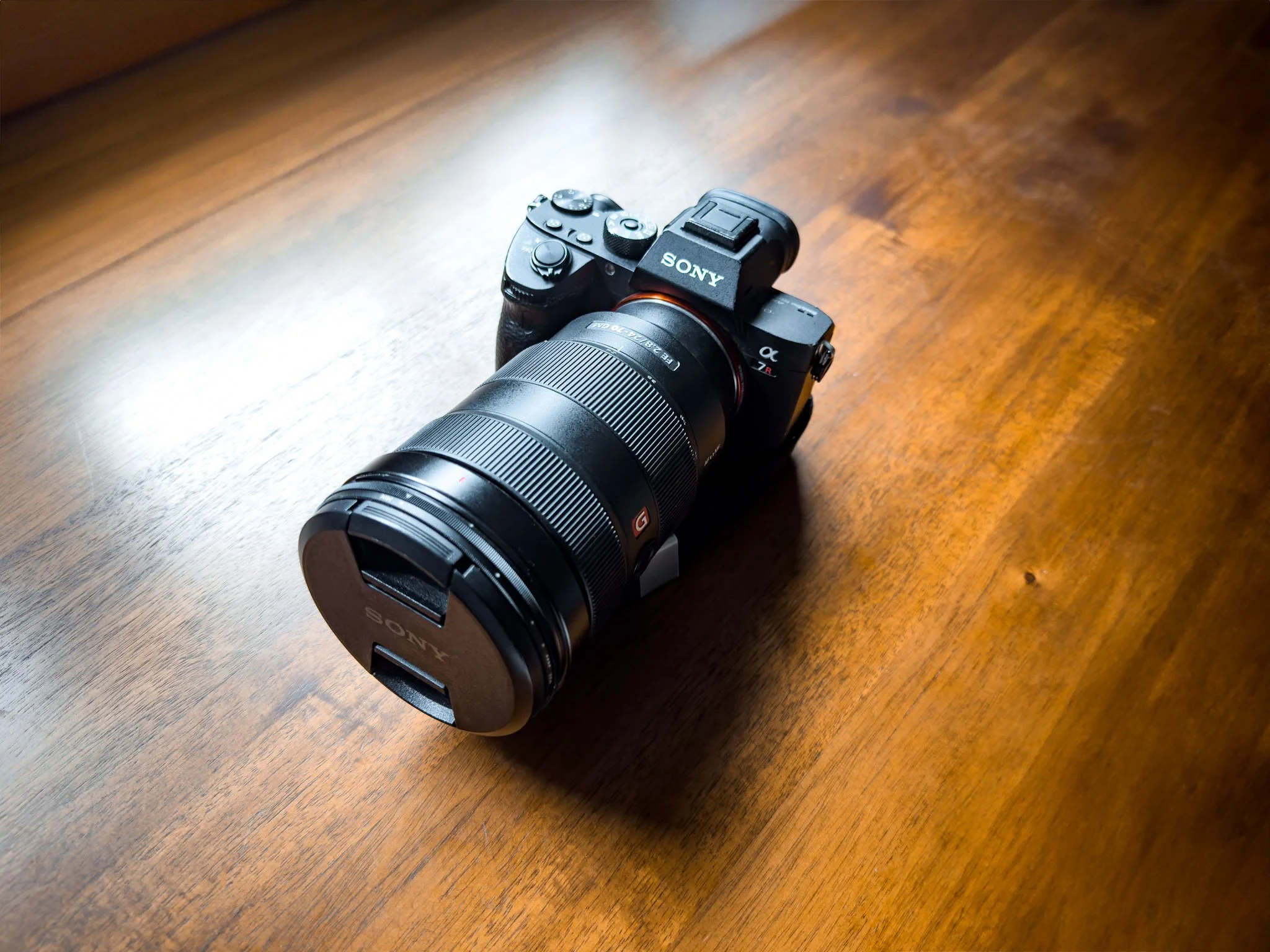 A Sony mirrorless camera with a large zoom lens resting on a wooden surface.