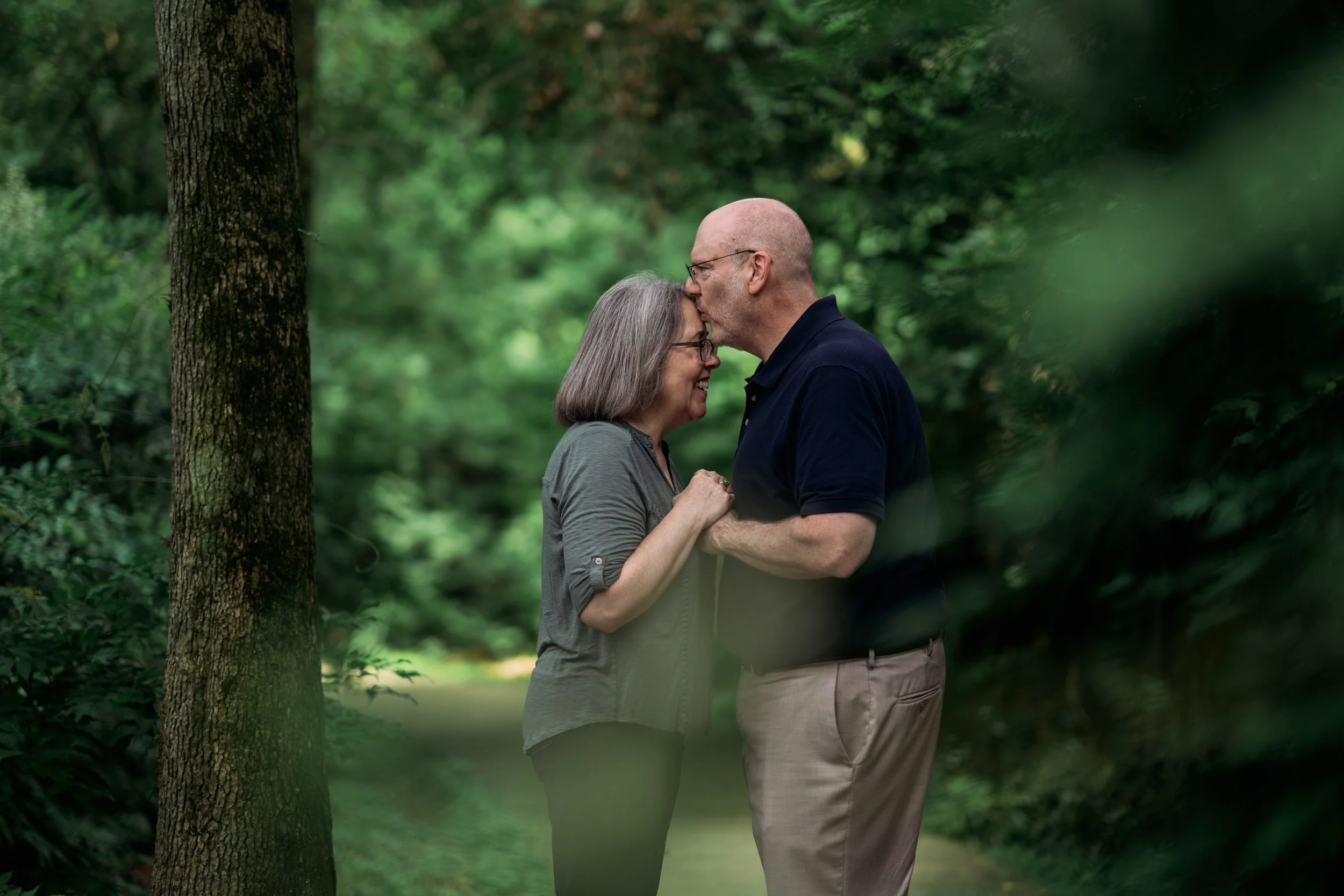 An elderly couple sharing a kiss in a lush, green forest.