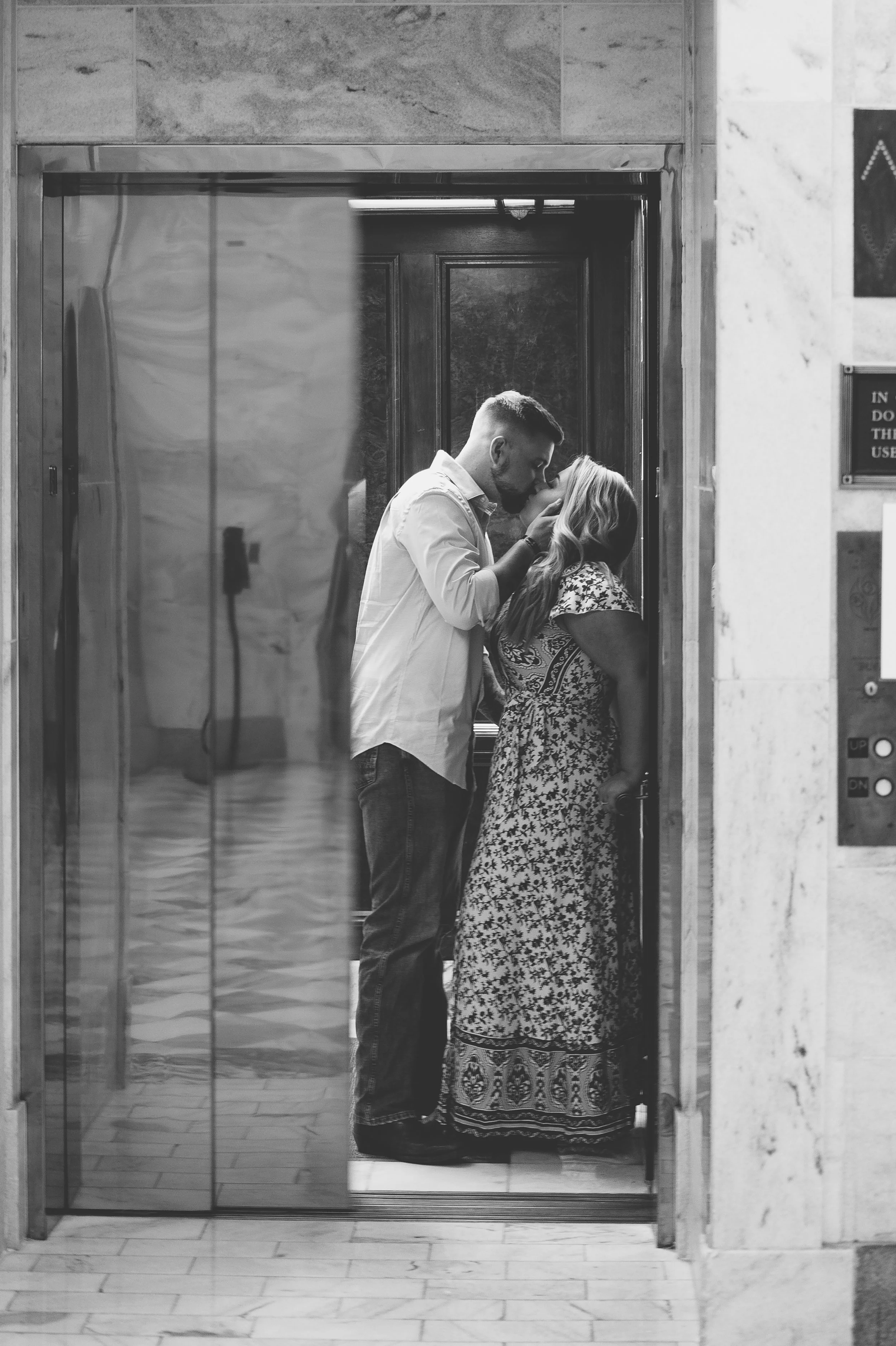 A man and woman in an elevator sharing a kiss, black-and-white photo.