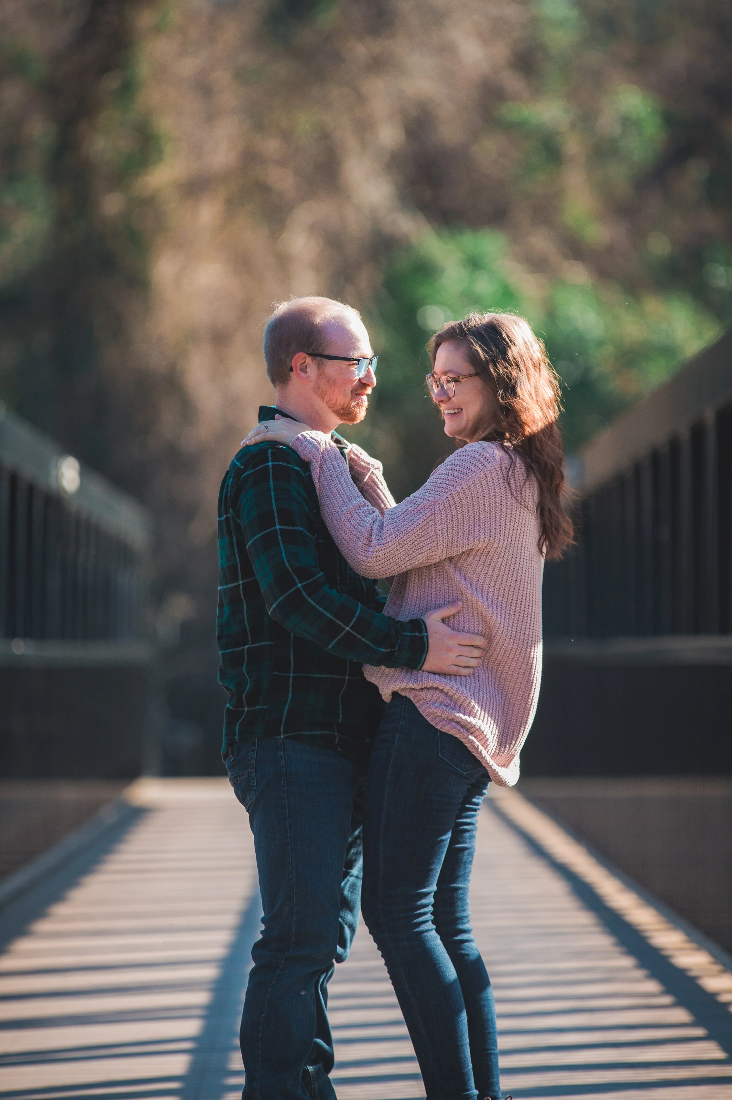 A couple sharing a joyful moment on a bridge outdoors, embracing each other and smiling.