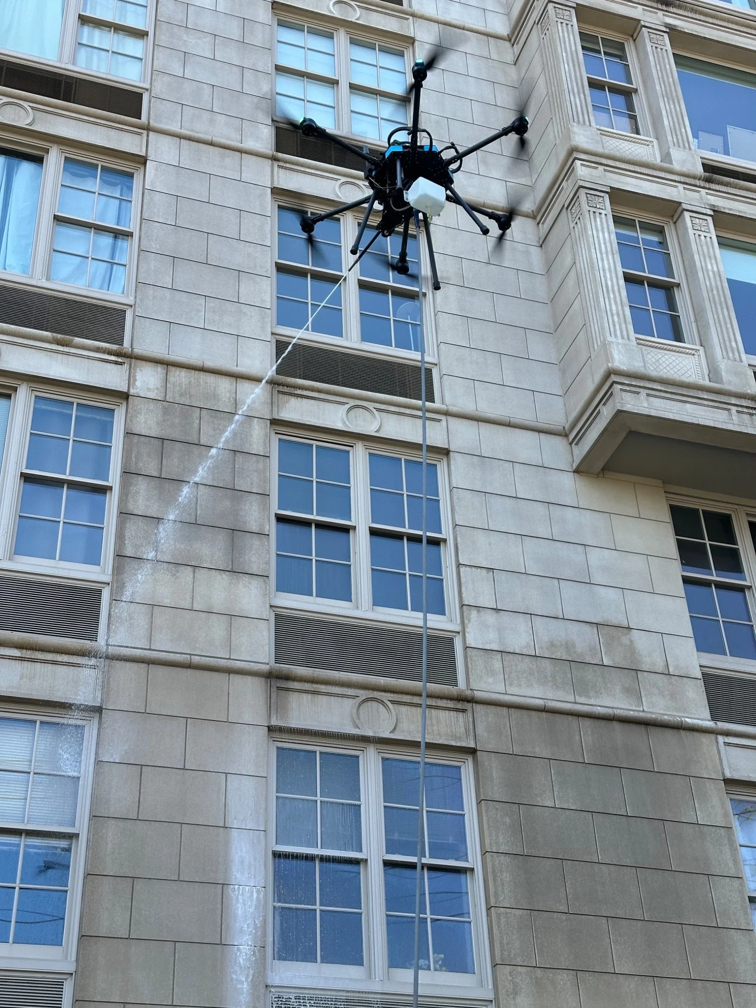 Close view of AeroShine’s cleaning drone beside the apartment facade during the 26,000-square-foot soft-washing project in Edgewater, NJ.