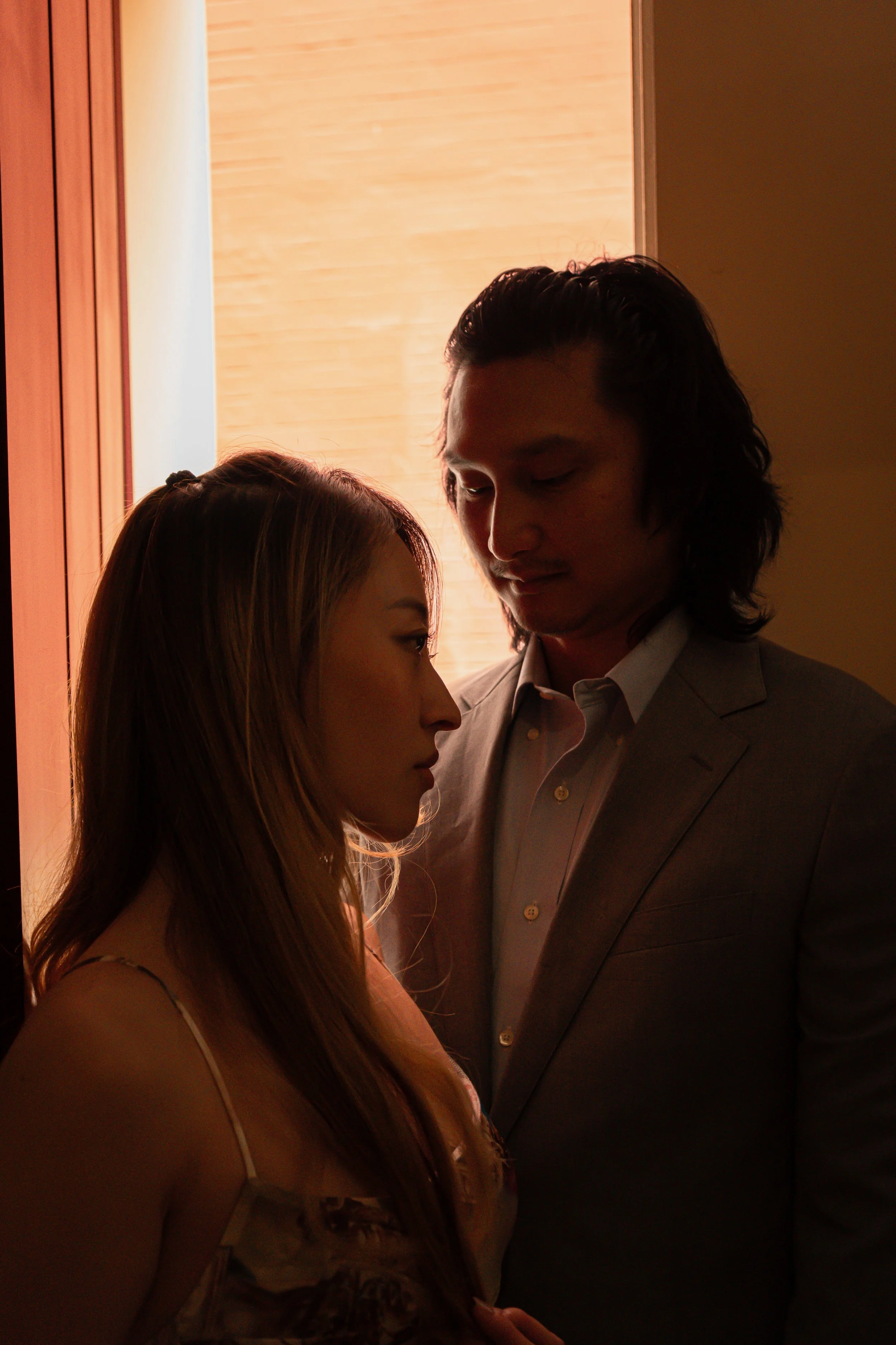 A man and woman face each other closely indoors near a window with warm light located in Seville, Spain.