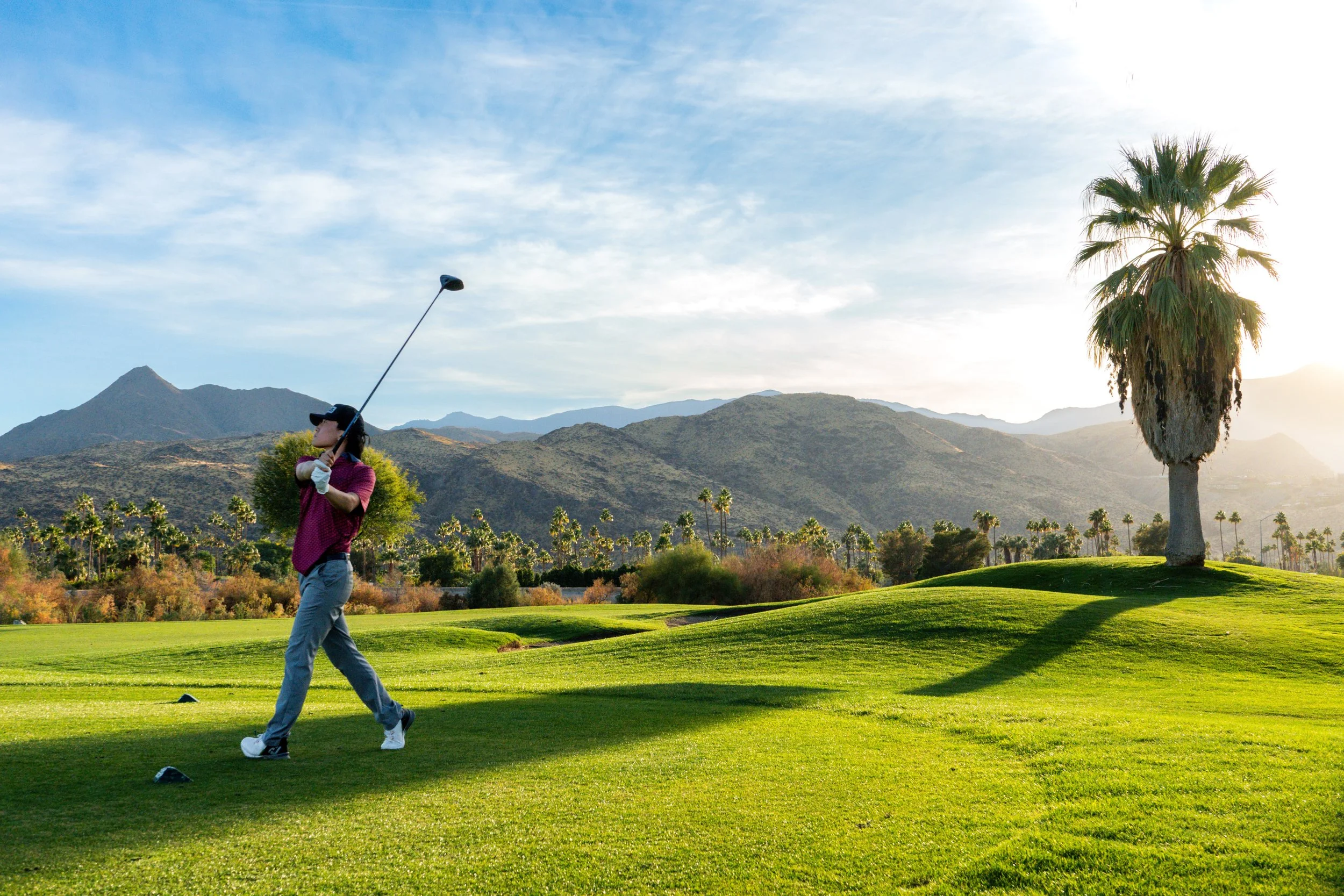 A woman playing golf on a lush green course with mountains and a clear sky in the background.