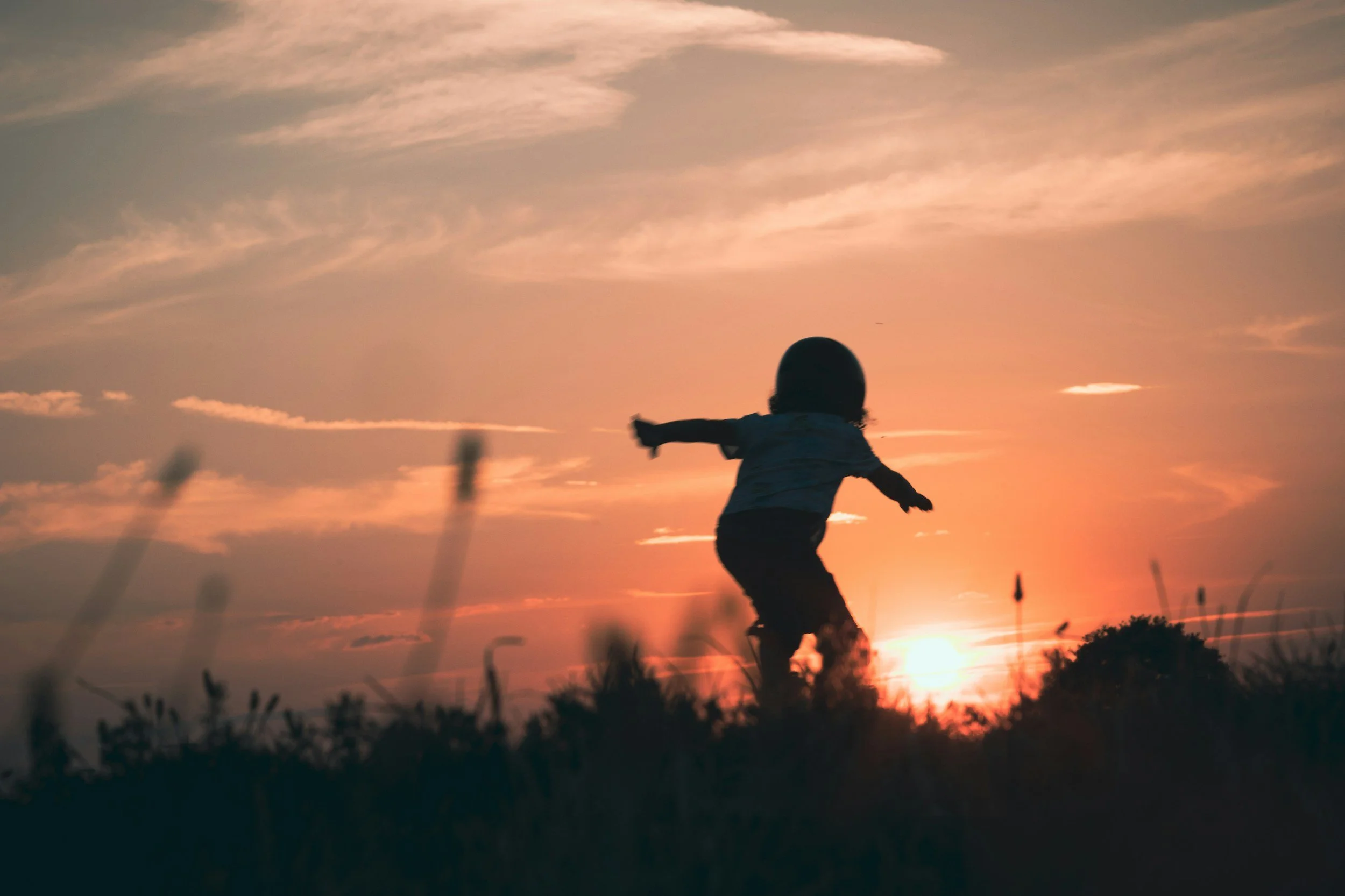 Silhouette of a small child in the middle of a field and looking toward the sunset, with knees bent and getting ready to jump
