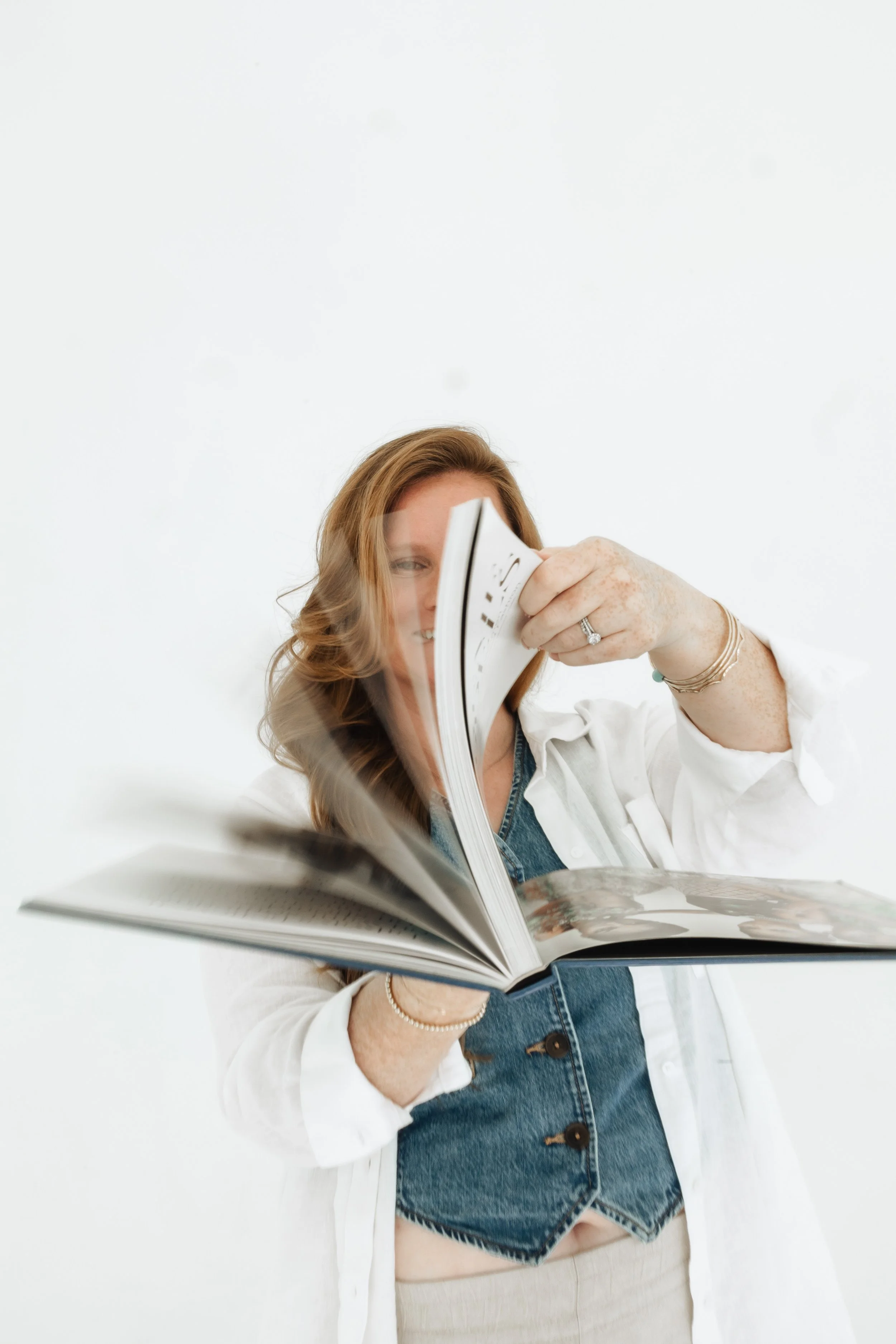 A woman with red hair flipping through a photo album against a white background.