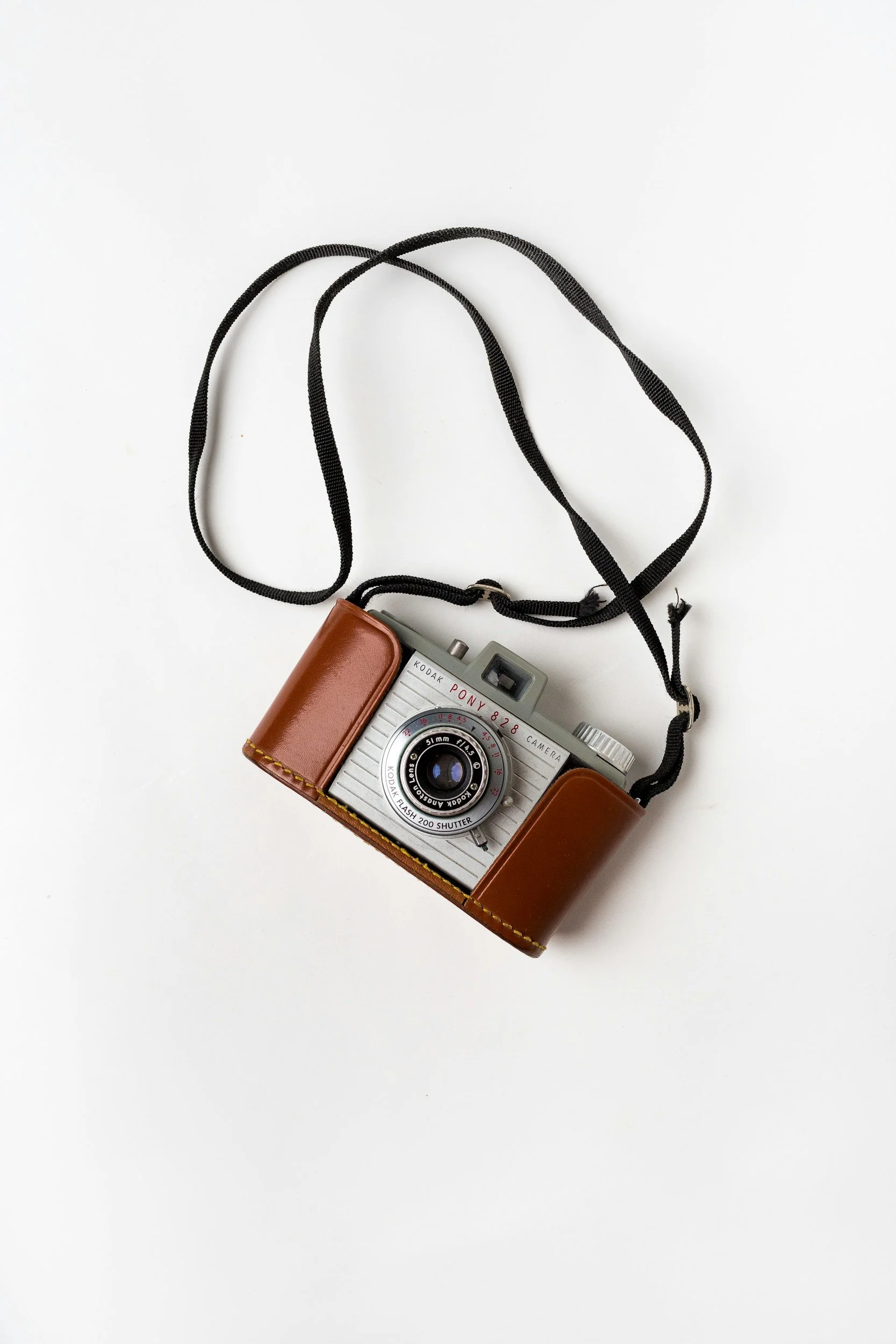 A vintage Kodak Pony 828 camera with a leather case and a black strap on a white background.