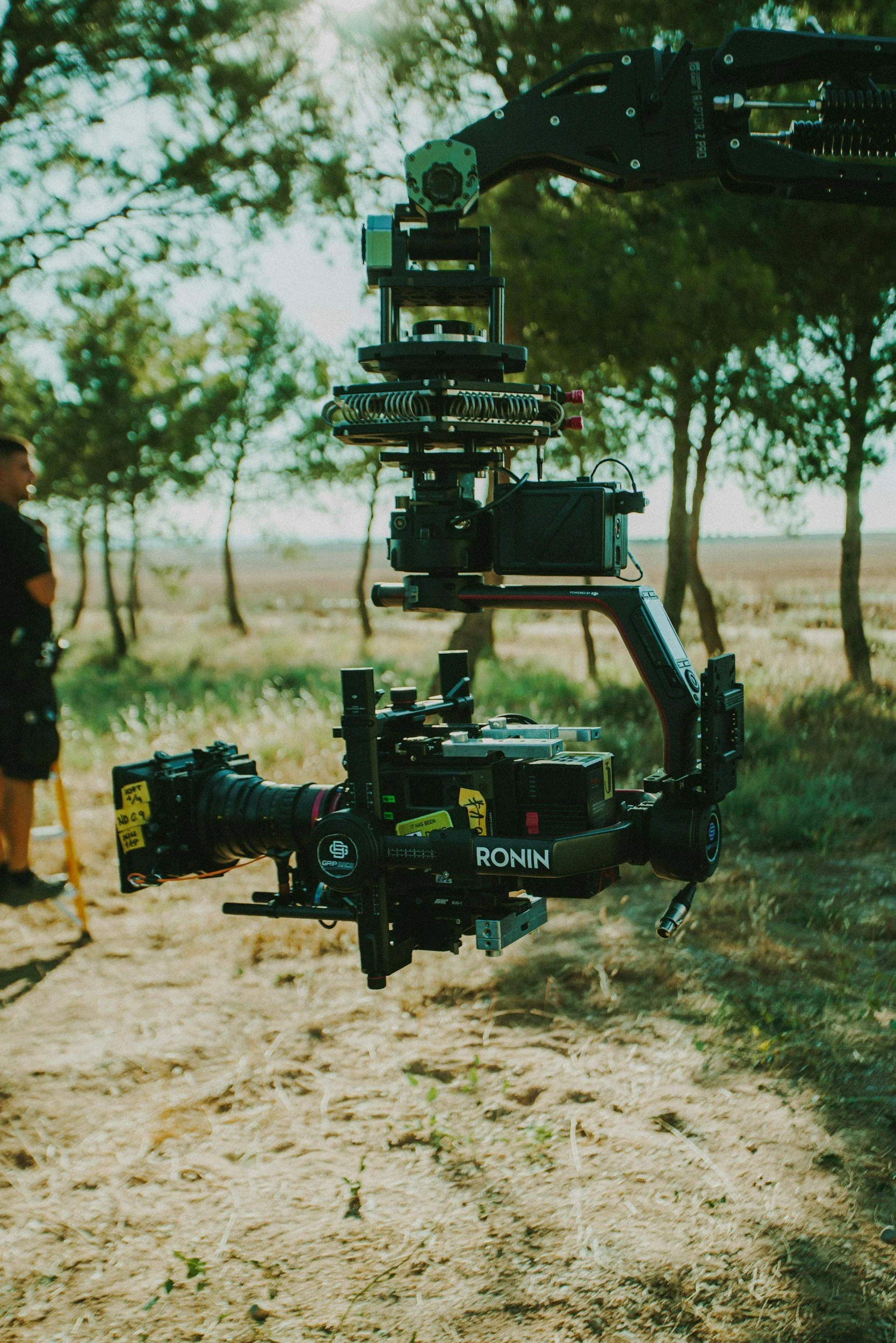 A professional camera mounted on a drone in an outdoor setting with trees and a dirt path.