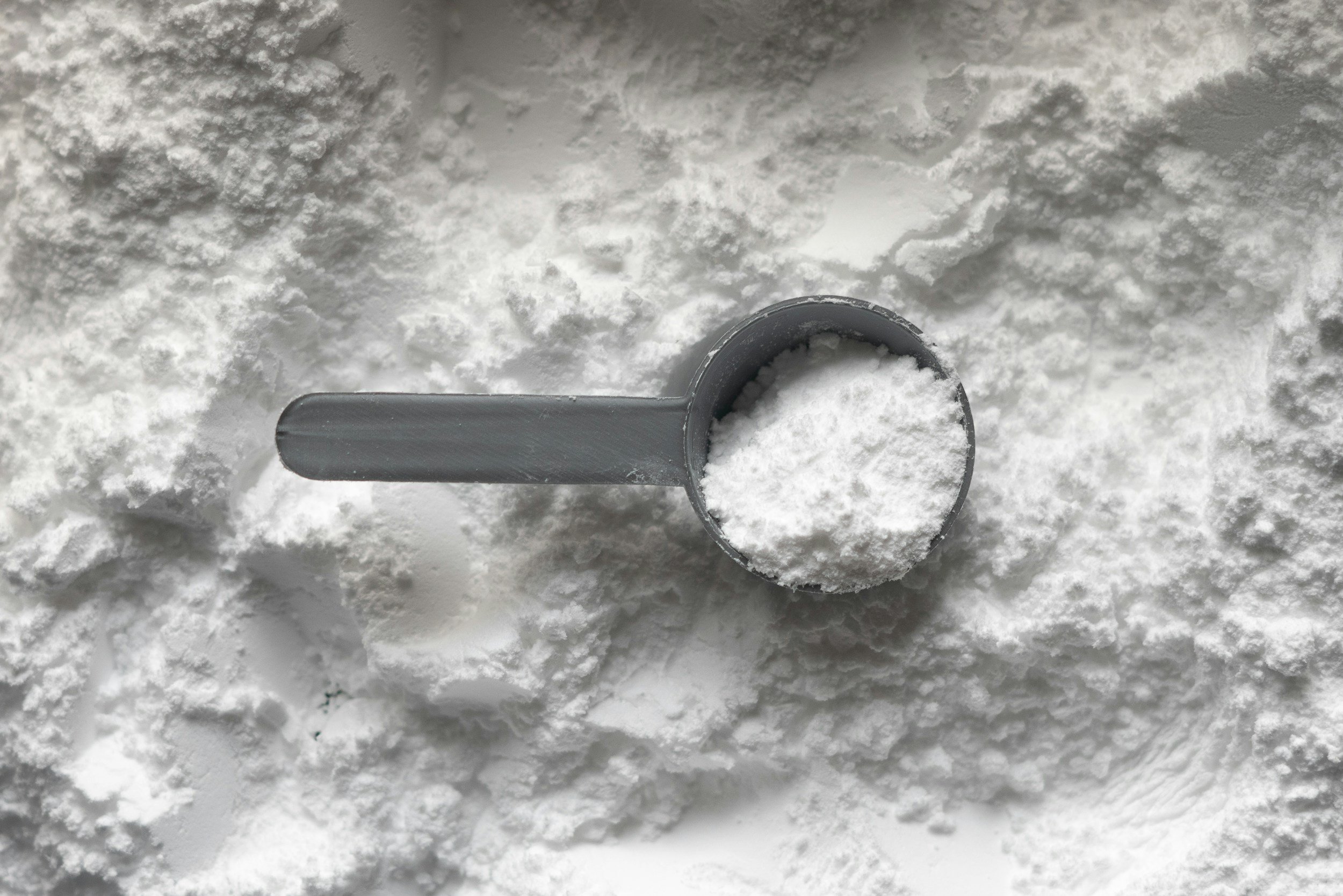A metal scoop filled with white powdered substance, surrounded by a surface of the same powder.