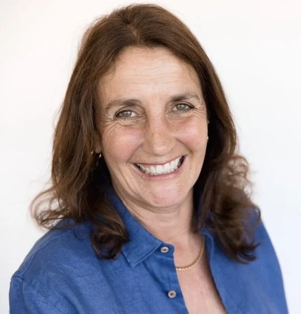 Smiling woman with brown hair in a blue shirt against a white background.