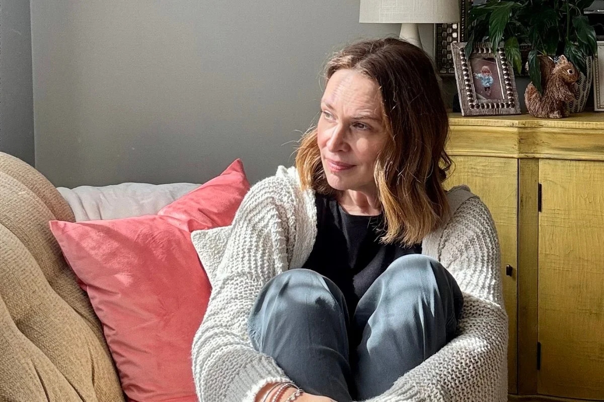 Valerie Gibson Jones, Christian Life and Leadership Coach, is sitting on a cozy sofa with her knees pulled to her chest. She's look contentedly out a nearby window with a kind, gentle smile.