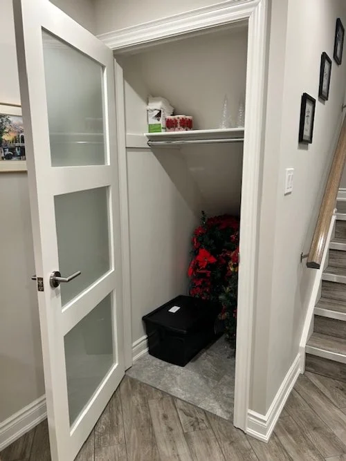 Small storage closet with a Christmas wreath inside, a black storage bin, and a shelf with tissue box and decorative items.