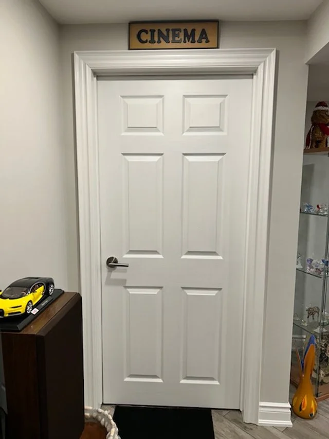 White door with a sign labeled 'CINEMA' above it, in a room with shelves on the right and a small table with a toy car on it on the left.