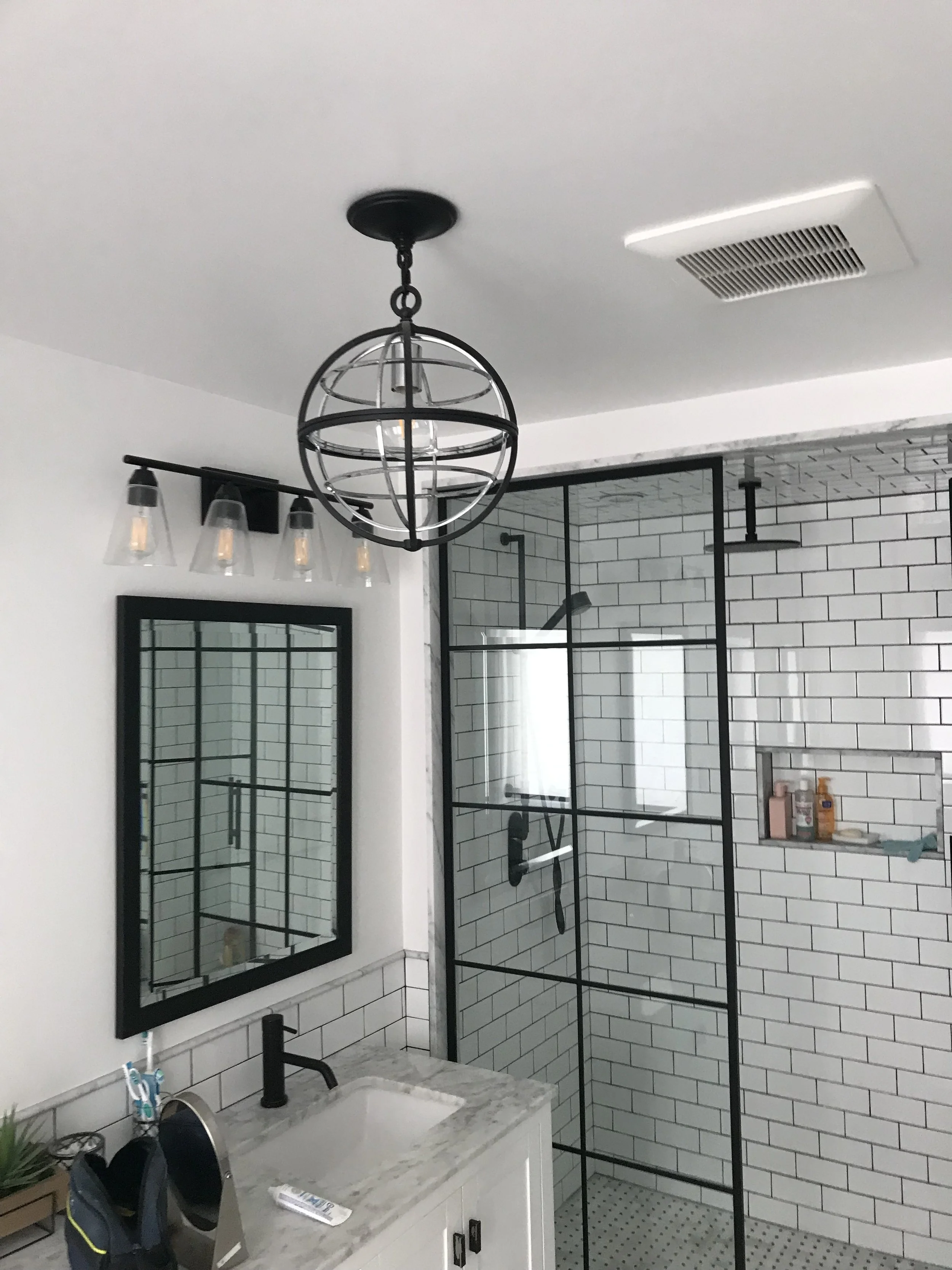 Modern bathroom with a marble countertop vanity, black-framed mirror, black fixtures, a pendant light, and a walk-in shower with white subway tile and black framing.