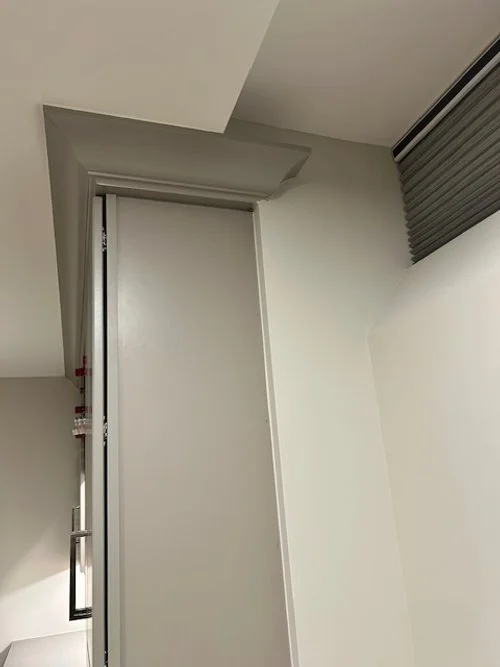 Interior room corner with a white wall, window with horizontal blinds, and ceiling with a drop ceiling detail.