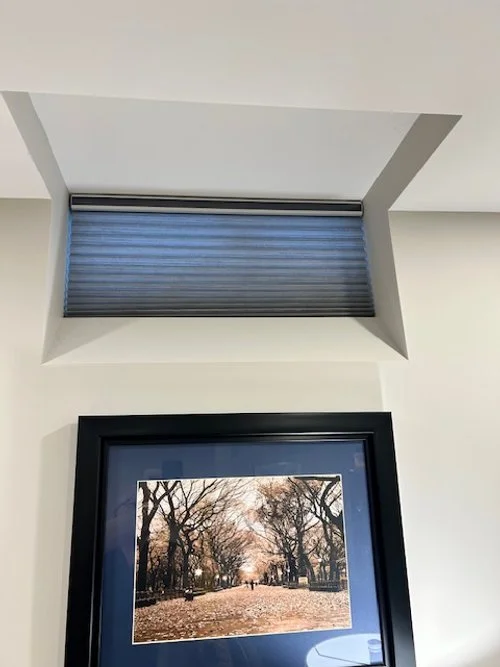 Ceiling window with a roller blind above a picture frame of a park with trees and a path.
