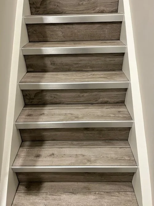 Interior view of a staircase with six steps, wood-like treads, and white risers beside white walls.