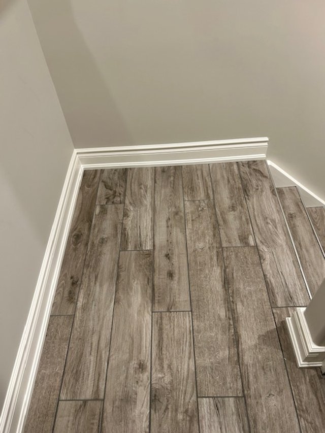 Top corner of a room with gray walls, white baseboards, and wood-look grey floor tiles.