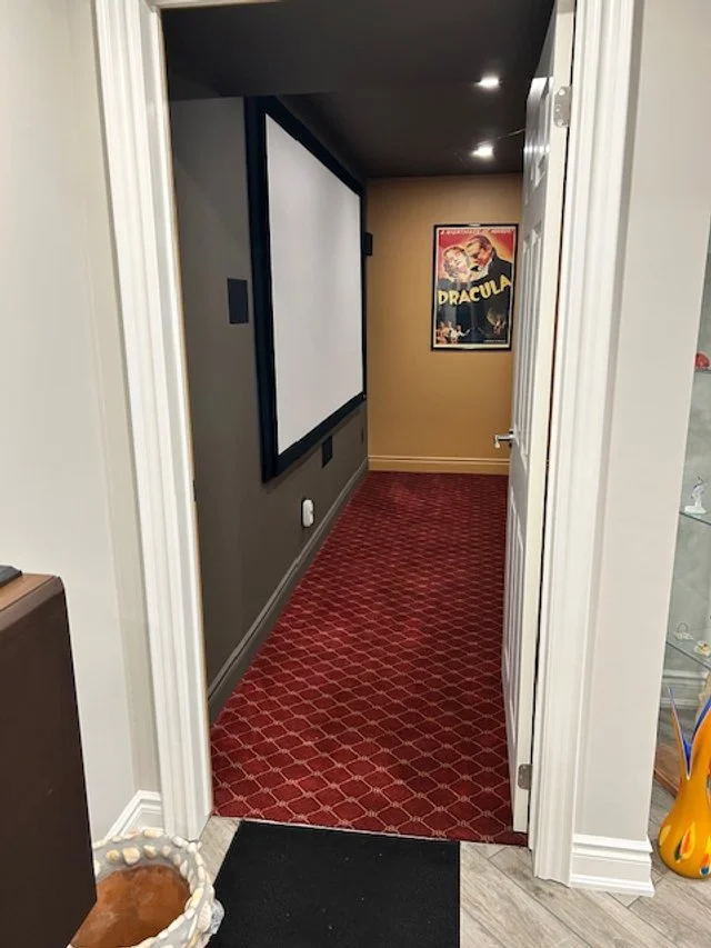 A hallway with a red geometric patterned carpet and beige walls, featuring a vintage horror movie poster on the far wall.