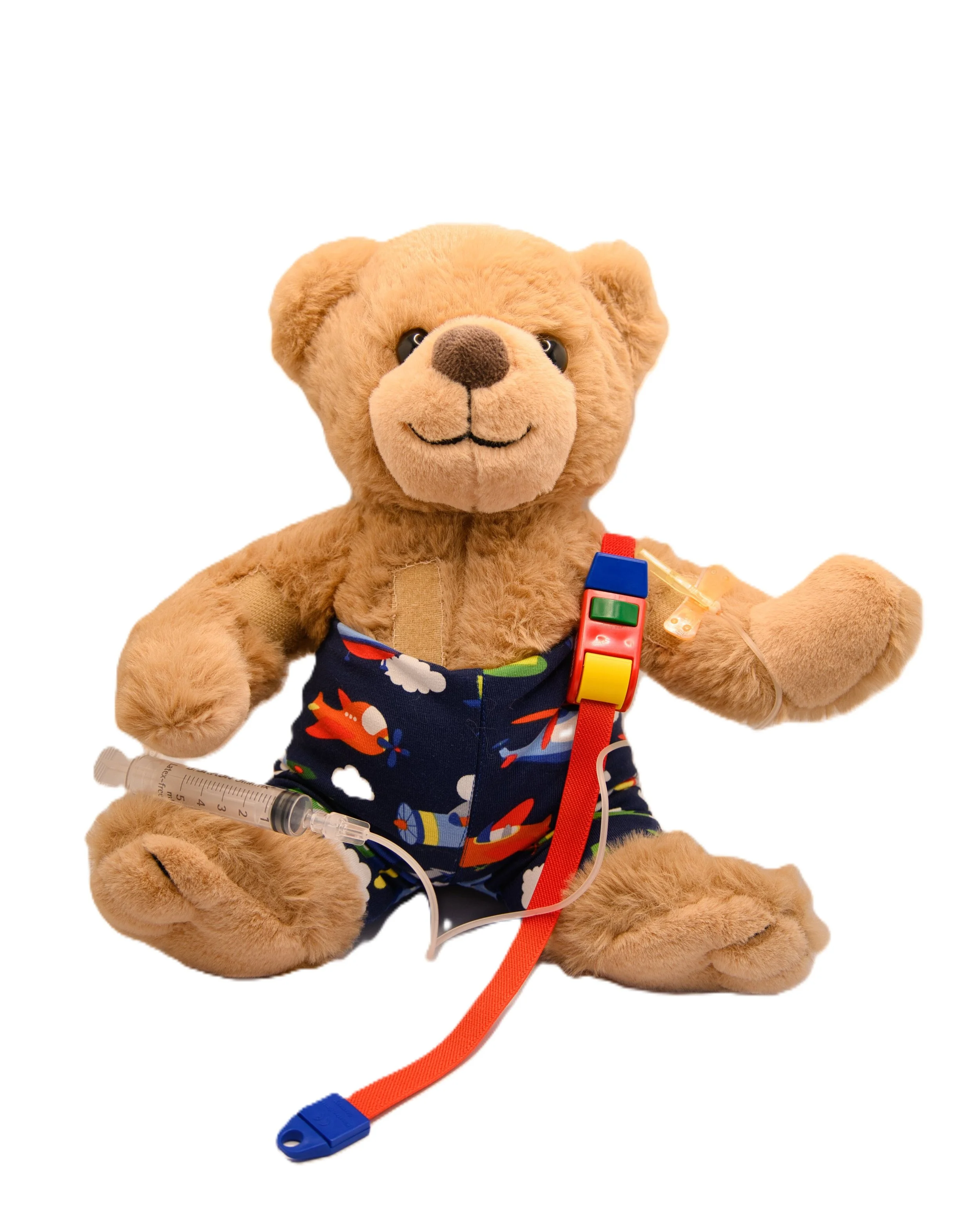 Teddy bear dressed in a colorful outfit with medical supplies attached, including a syringe and stethoscope, sitting on a white background.