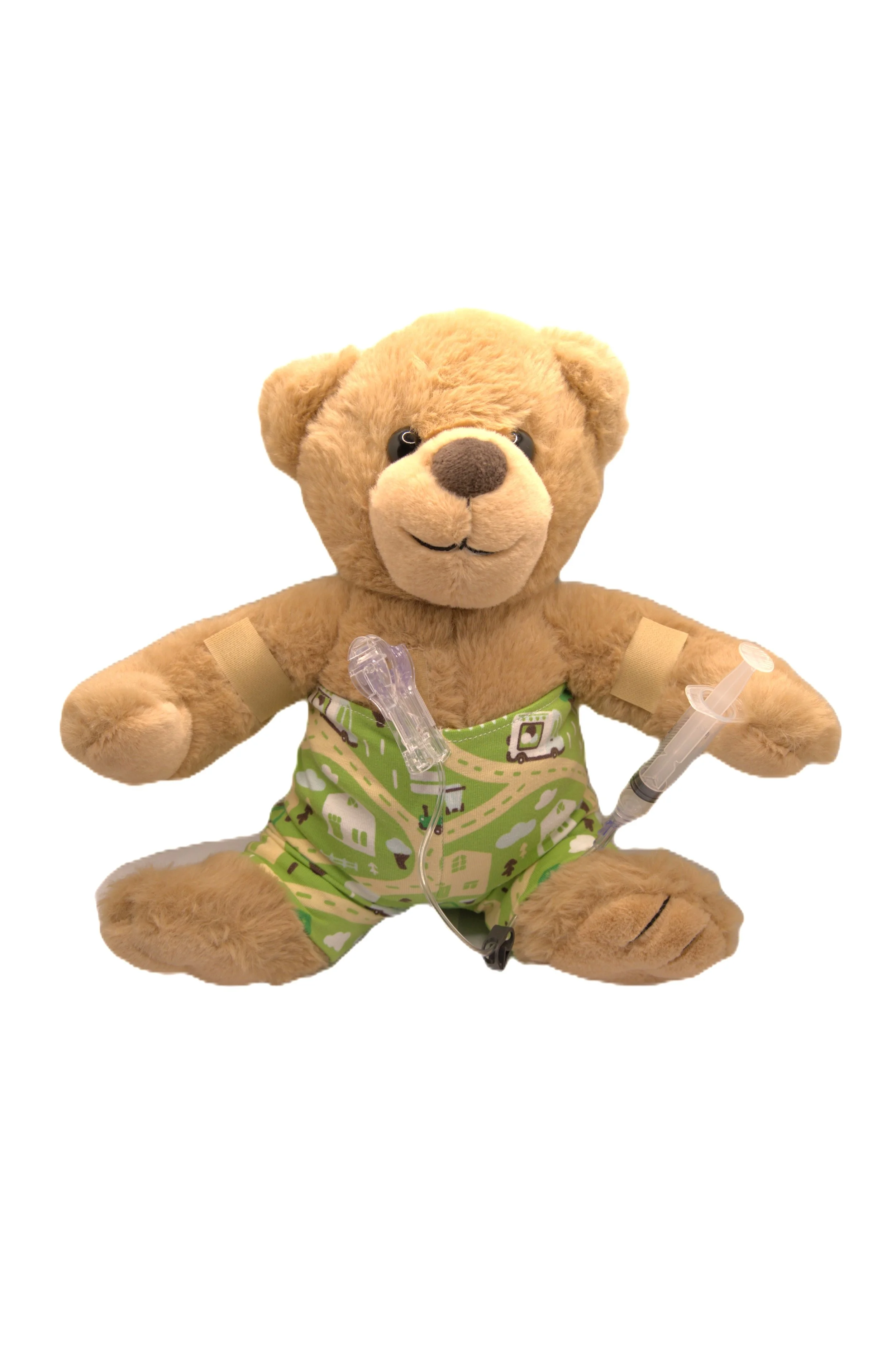 Teddy bear plush toy dressed in green pajamas with a road pattern, sitting against a white background, with medical equipment including a pulse oximeter and syringe attached.
