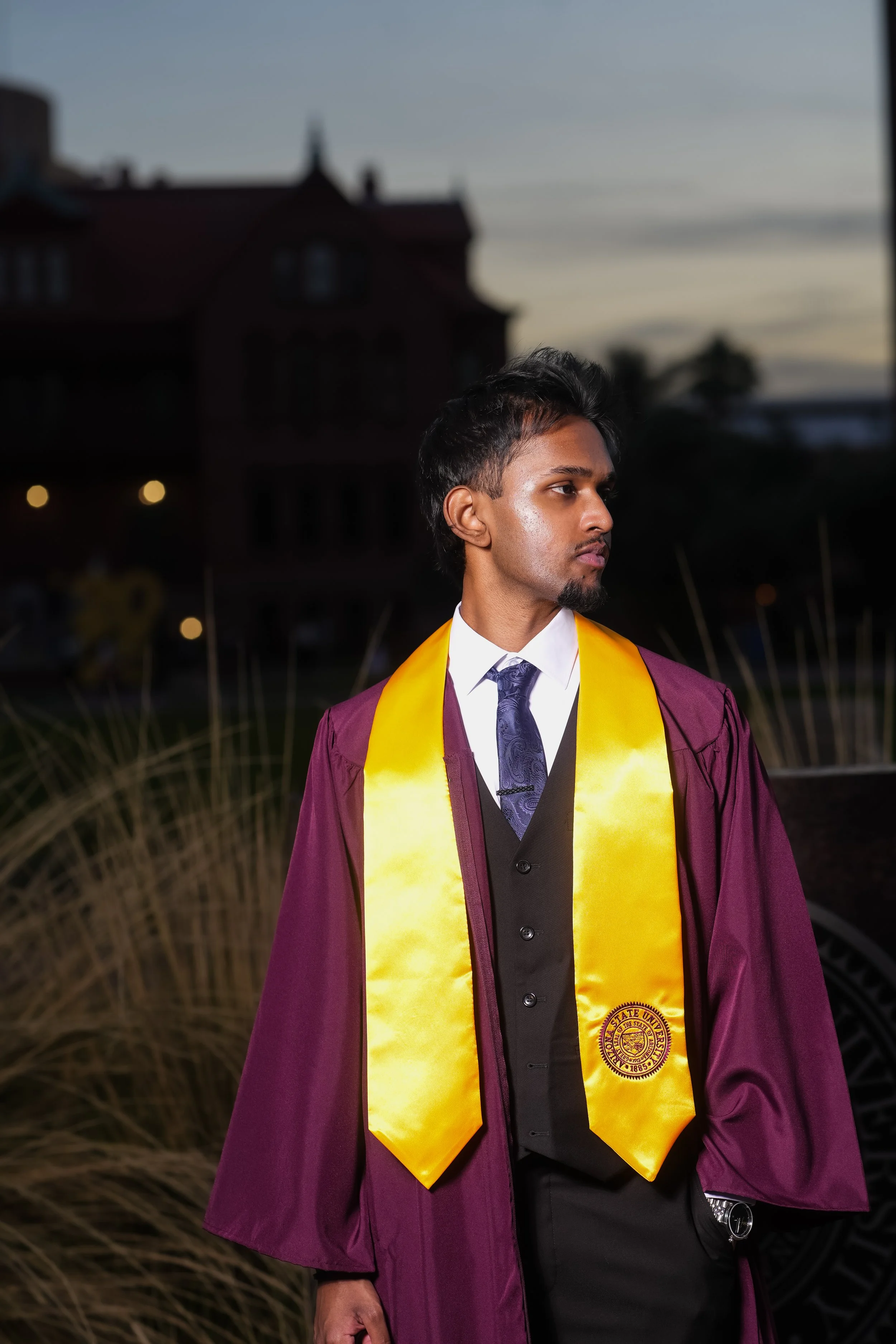 Arizona state graduate; Man in suit adjusting jacket on Phoenix, Arizona rooftop with sunset background.