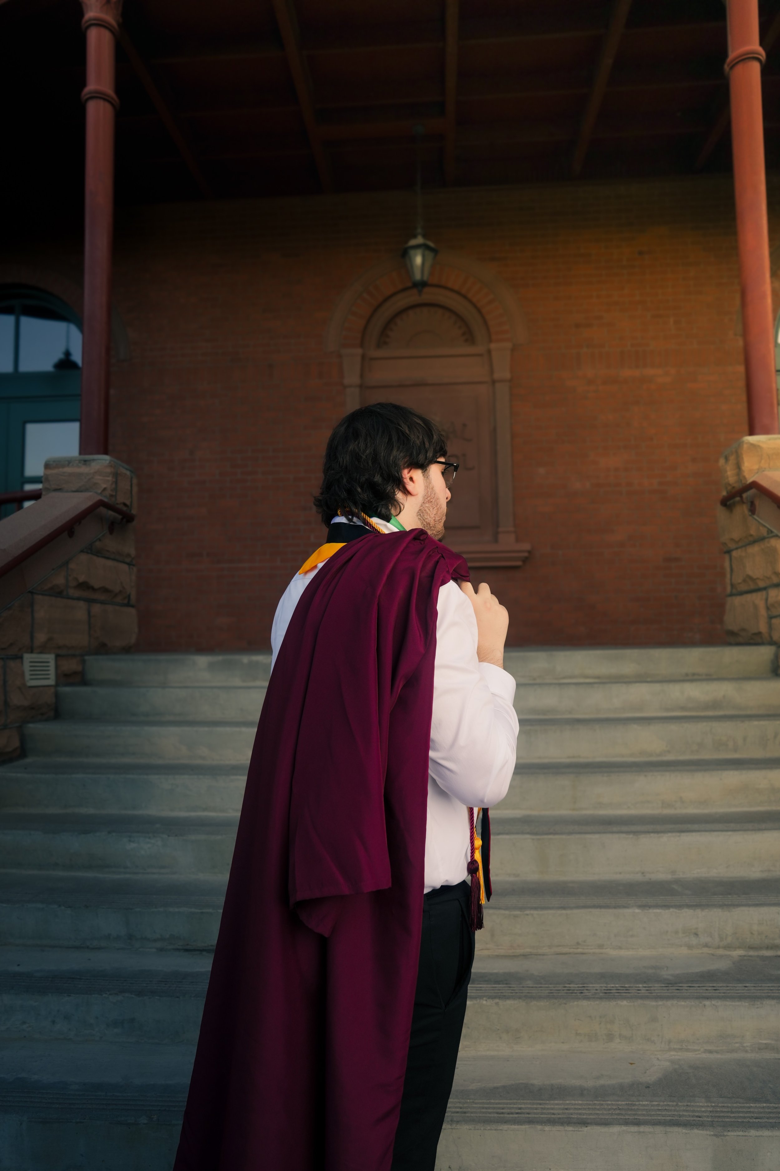 Arizona state graduate; Man in suit adjusting jacket on Phoenix, Arizona rooftop with sunset background.