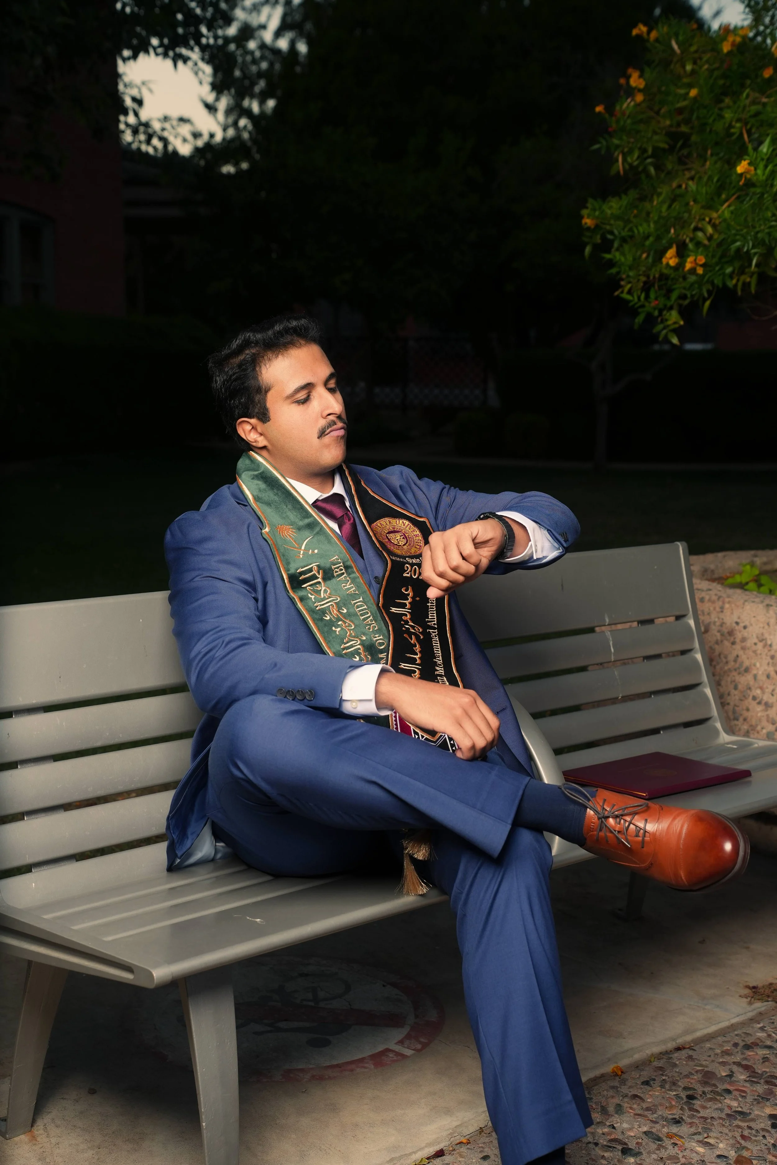 Arizona state graduate; Man in suit adjusting jacket on Phoenix, Arizona rooftop with sunset background.