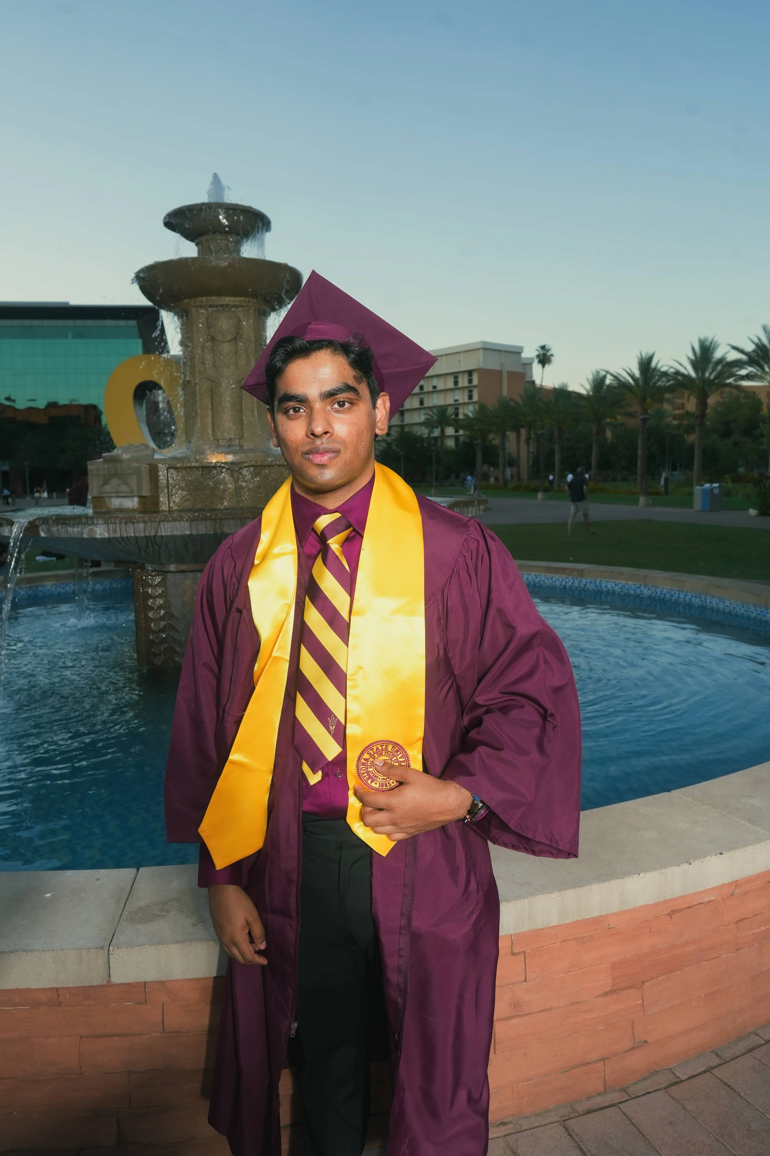 Arizona state graduate; Man in suit adjusting jacket on Phoenix, Arizona rooftop with sunset background.