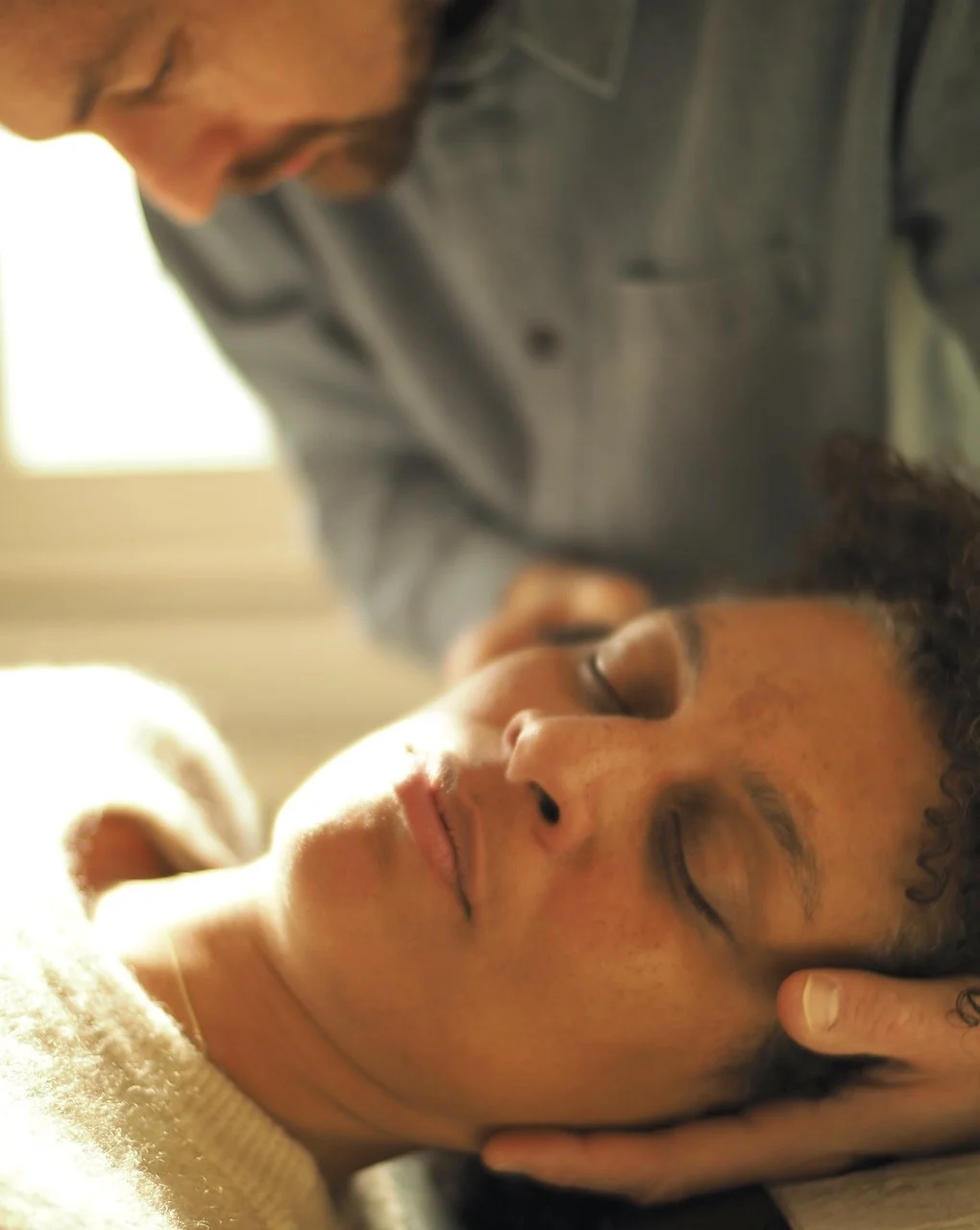 Ein Mann, der sanft den Kopf einer entspannten Frau hält, möglicherweise in einer therapeutischen oder entspannenden Umgebung.