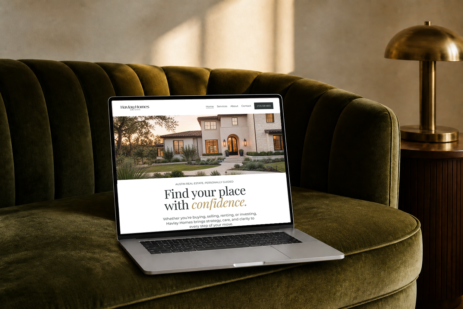 Laptop on green velvet sofa displaying a real estate website for Havlay Homes in front of warm indoor lighting.
