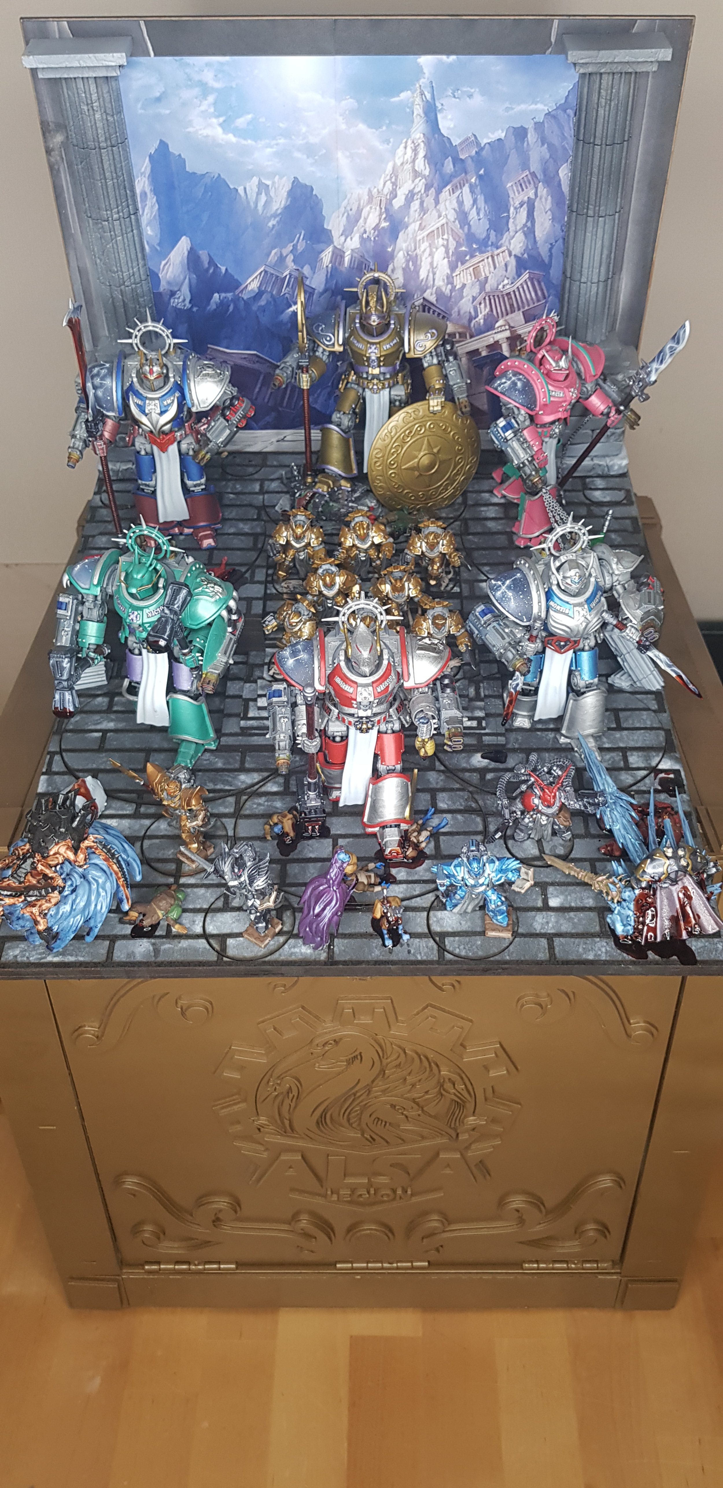 Une collection de figurines de guerriers et de créatures, inspirés de jeux vidéo ou de fantasy, sur un meuble orné d'un griffon. En arrière-plan, une scène de montagnes et de temples anciens.