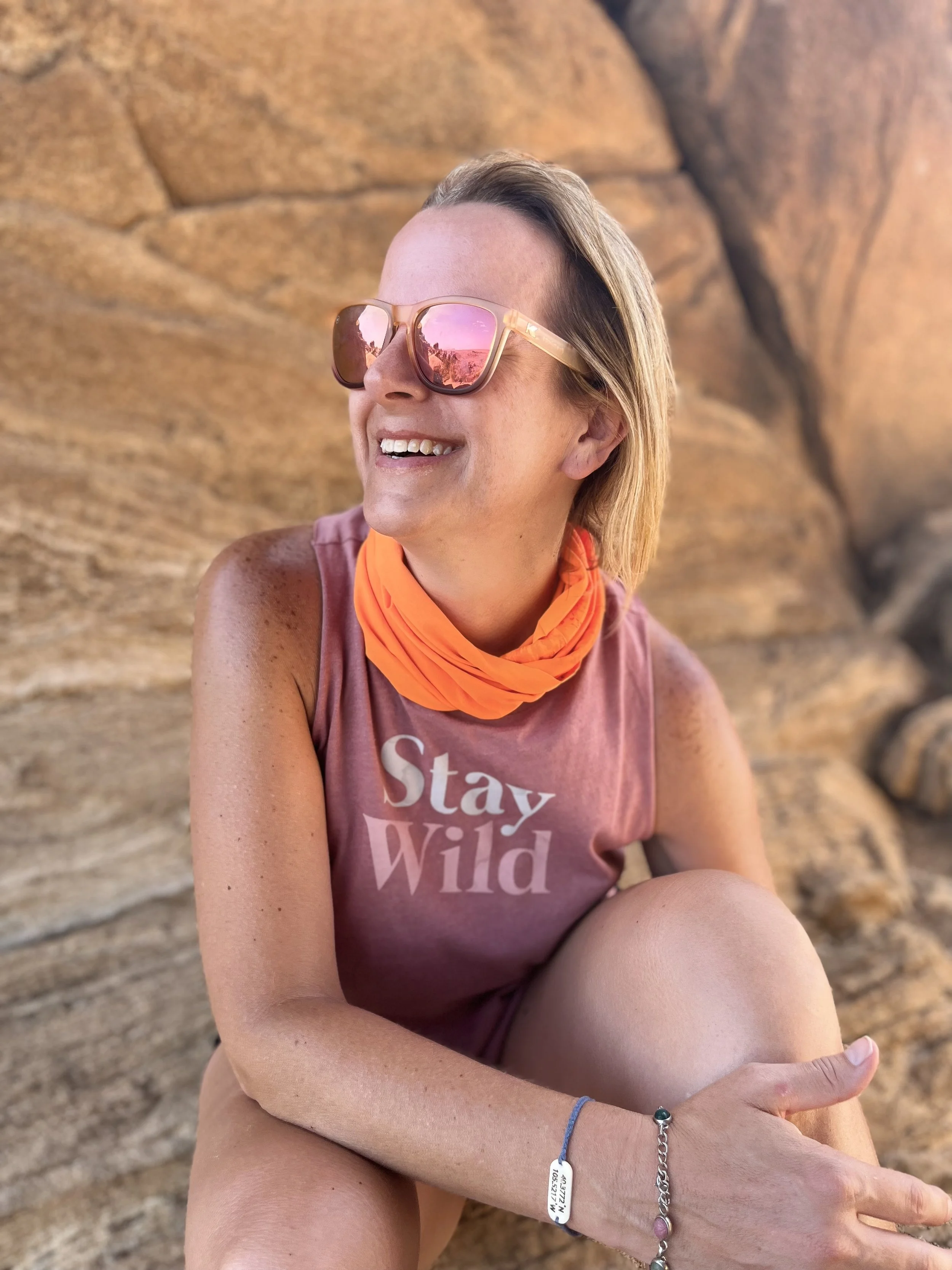 A woman smiling in front of a wooden wall with posters, wearing a sleeveless black dress with white polka dots.