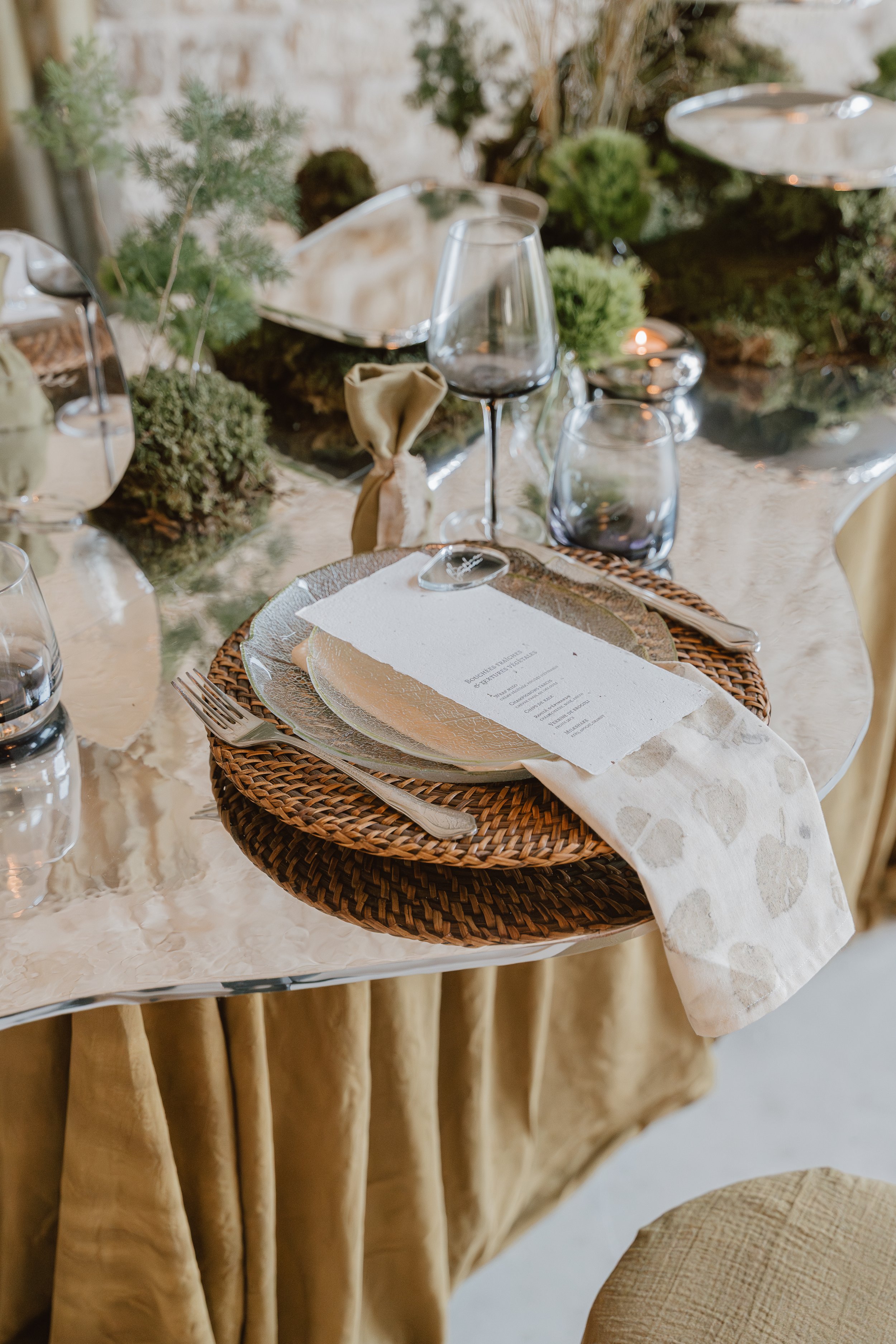 Une table de dîner élégante avec des assiettes, des couverts et des verres, décorée avec des éléments verts et une nappe beige.