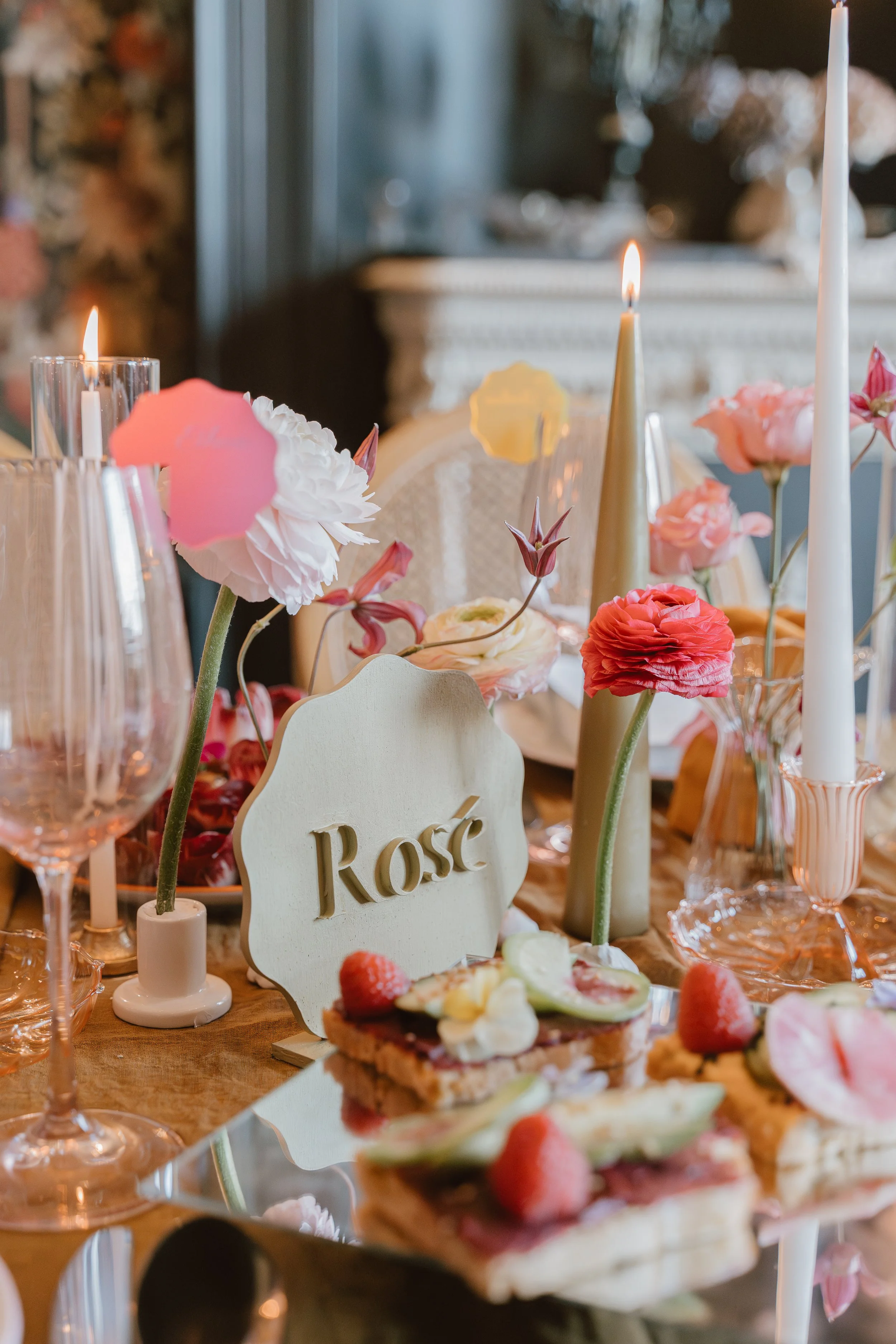 Table de fête avec fleurs roses, bougies, desserts et un panneau avec le mot 'Rosé'.