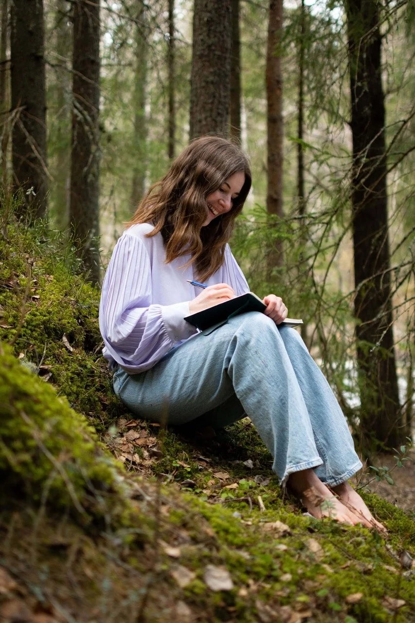 Bambisites Vilma kirjoittamassa muistivihkoon metsässä.