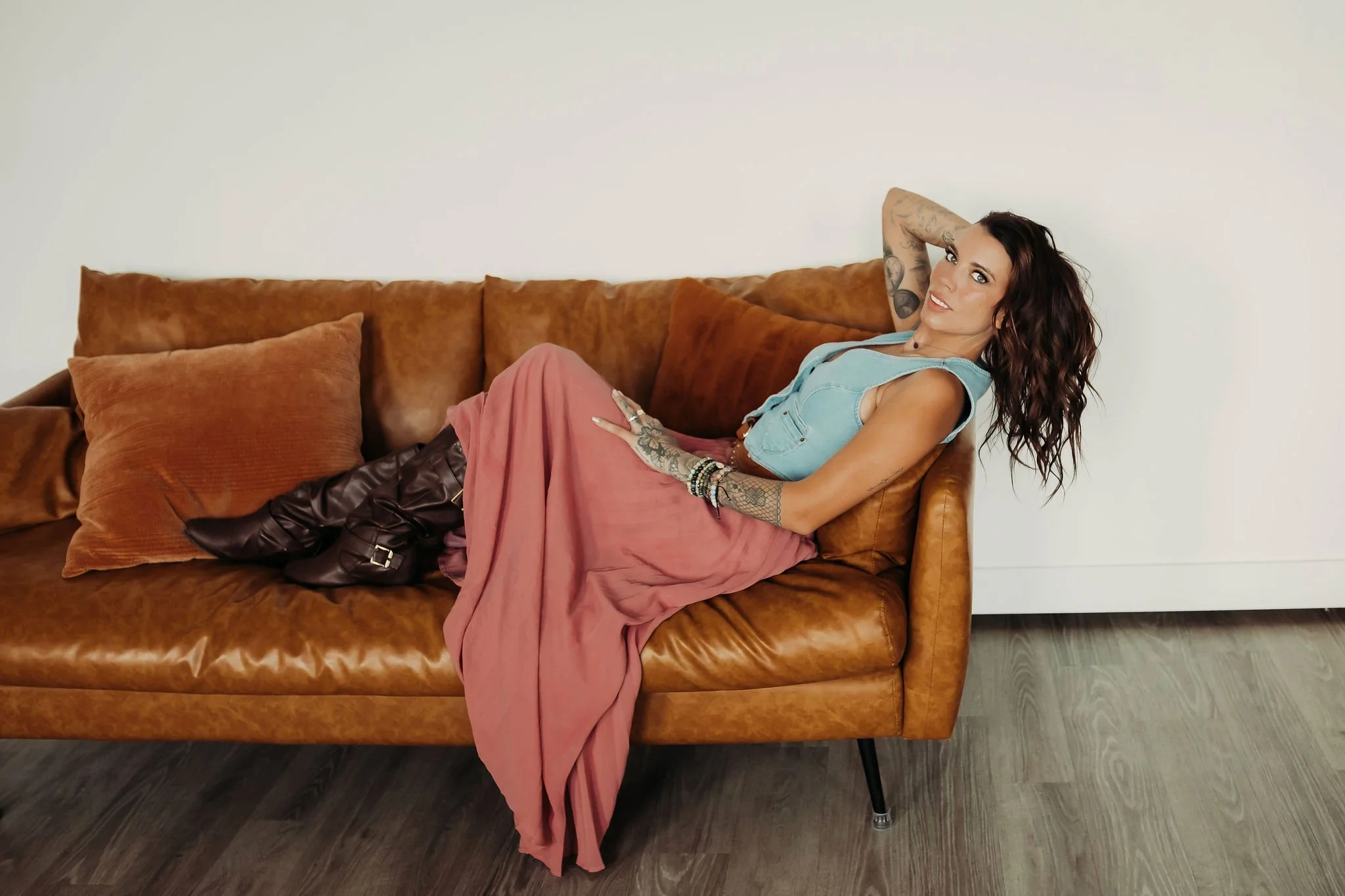 Woman with tattoos lying on a brown leather couch in a room with wooden floor