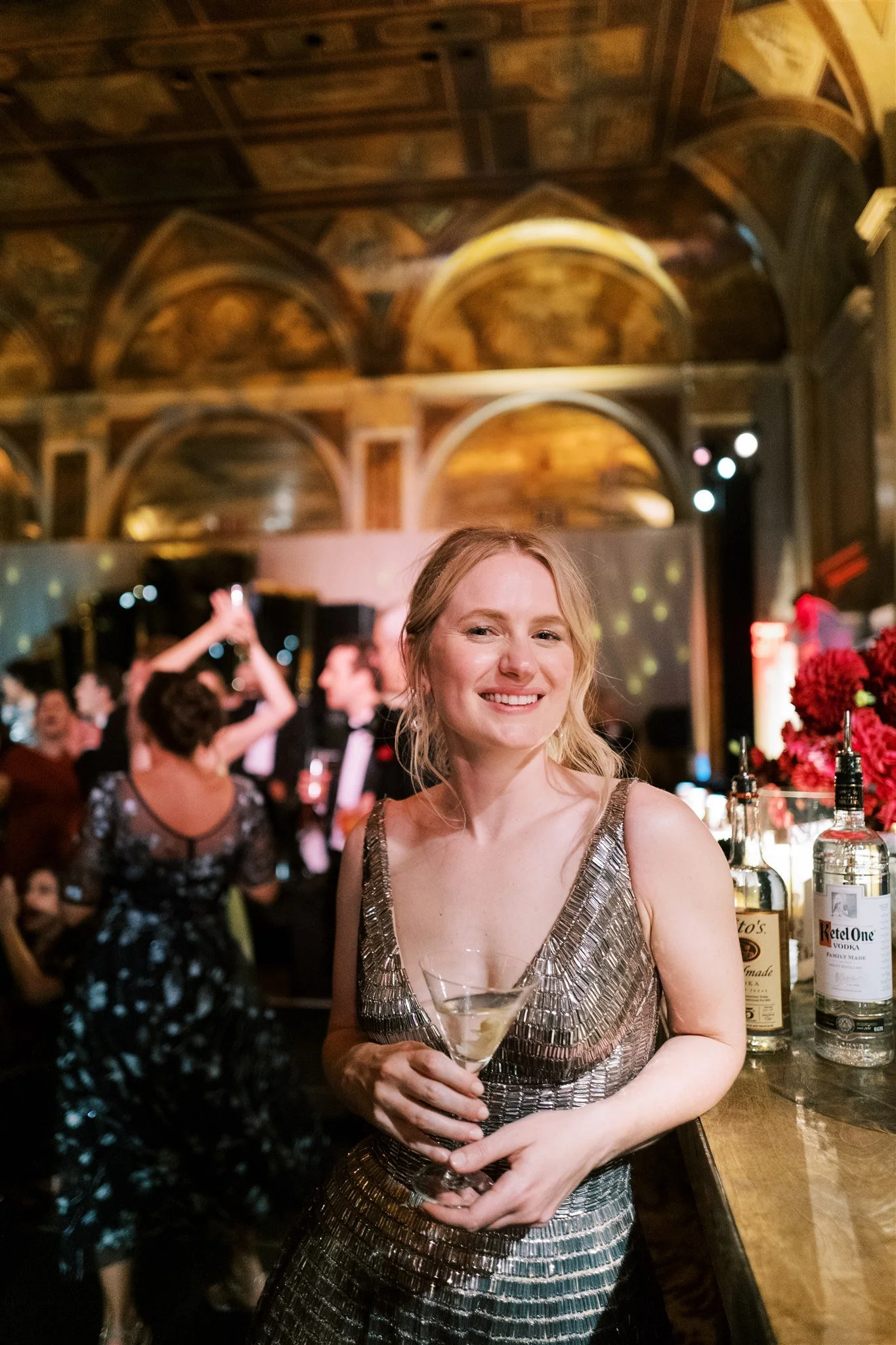 Bride smiles holding a martini glass at the reception bar surrounded by golden décor. plaza hotel wedding new york city.