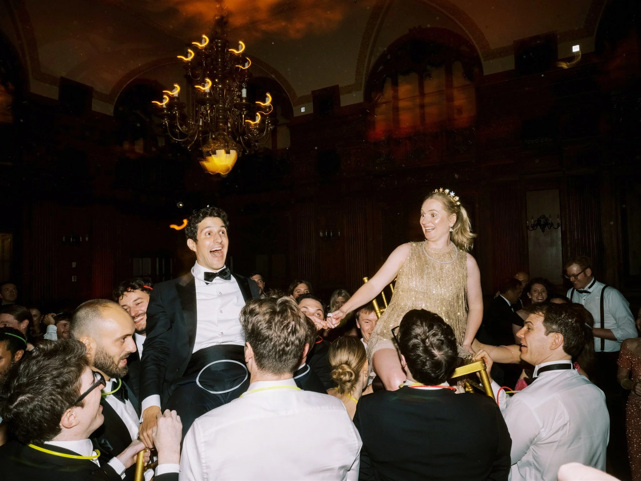 Bride and groom lifted in chairs during the Hora surrounded by guests celebrating. the plaza hotel new york luxury wedding.