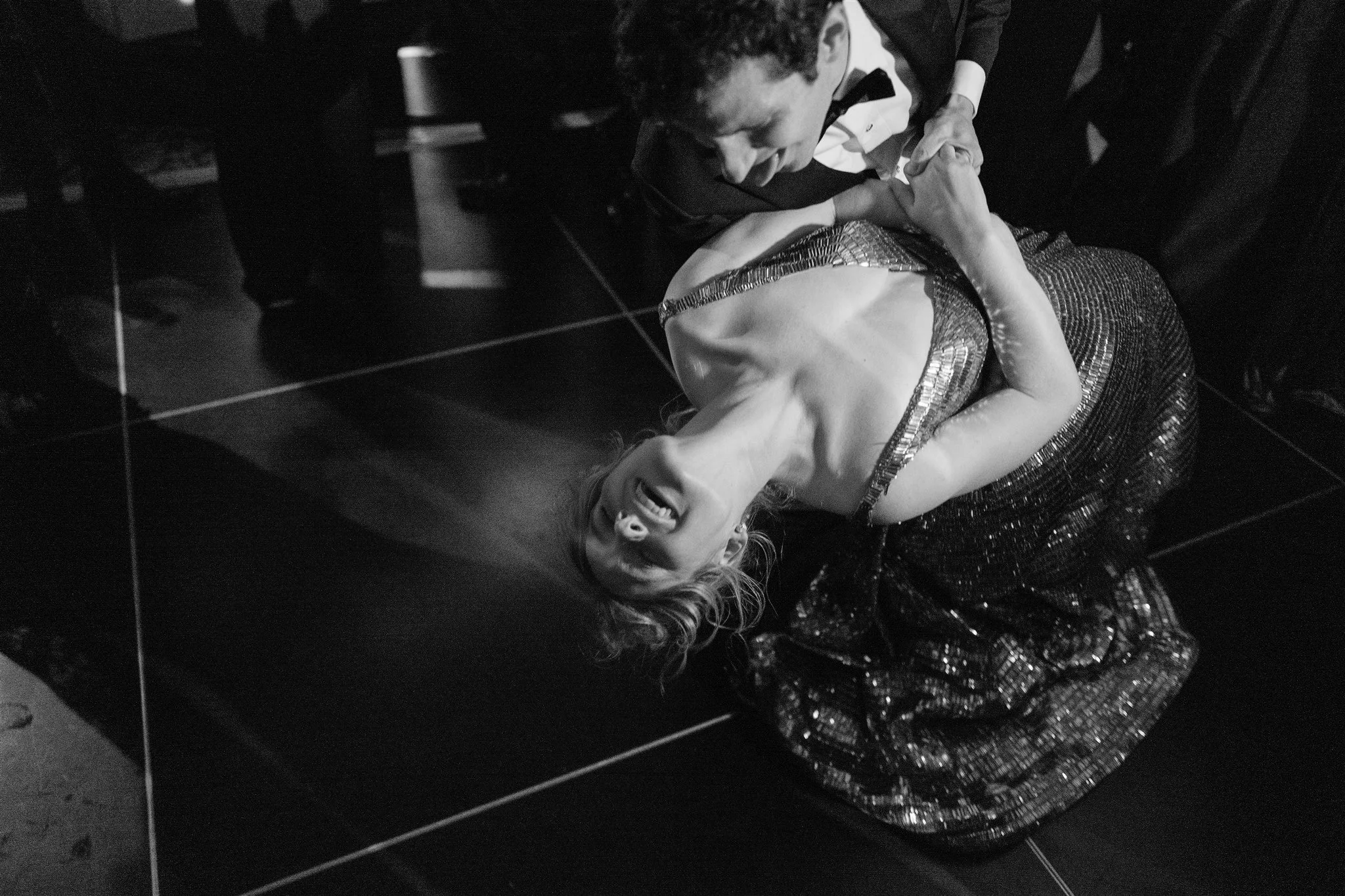 Groom dips the bride dramatically on the dance floor, her sequin gown sparkling under the lights. manhattan wedding photographer new york.
