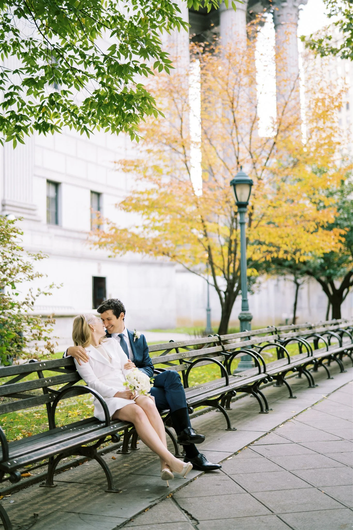 The couple cuddles on a park bench surrounded by autumn color. manhattan wedding photographer new york.