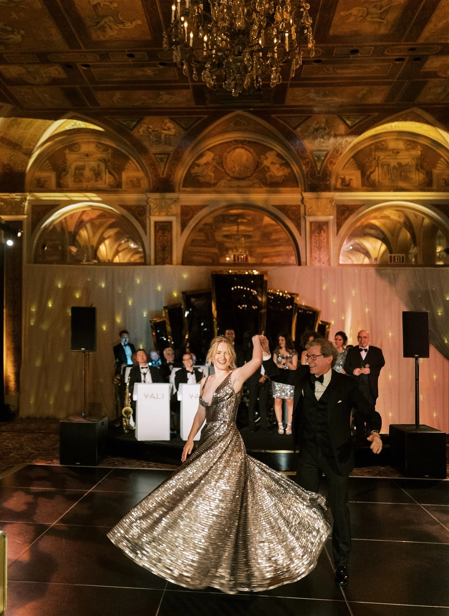 Bride and her father dance beneath chandeliers in a gilded ballroom filled with laughter and applause. nyc The Plaza hotel wedding.