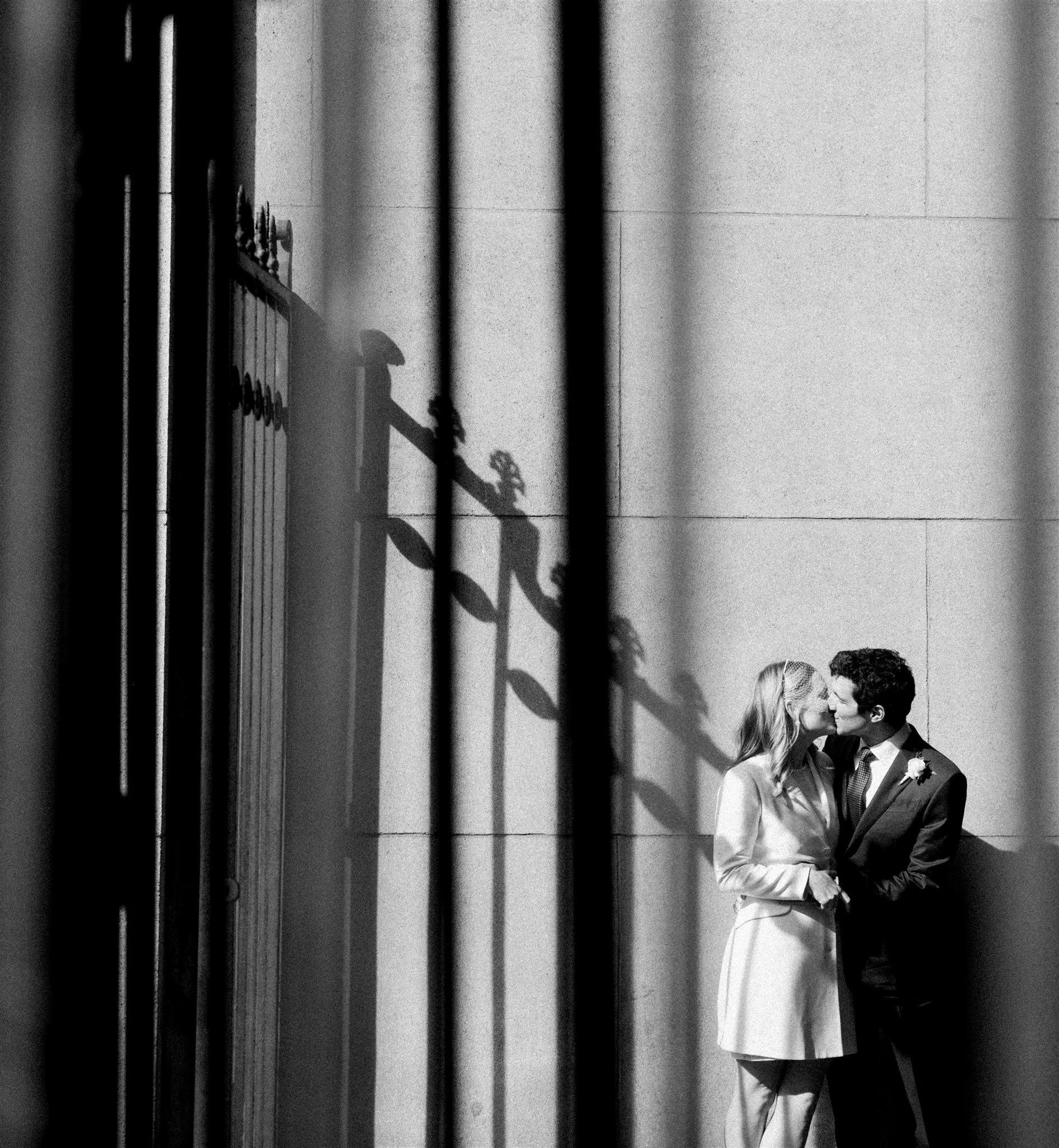 Artful black‑and‑white kiss framed by iron shadows on stone. michelle rago destinations plaza hotel wedding.
