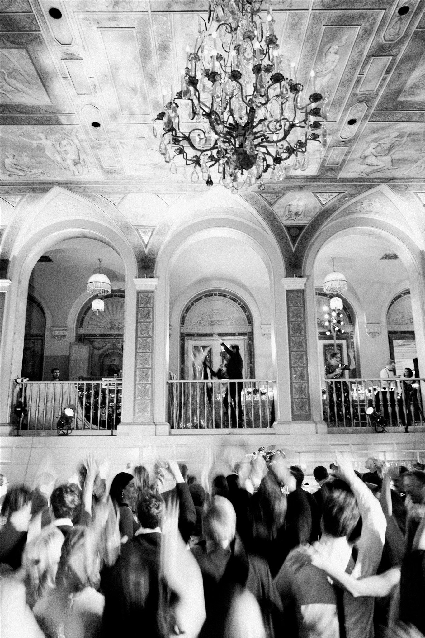 Ornate chandelier and frescoed ceiling above a crowded dance floor at The Plaza. editorial nyc wedding photography.